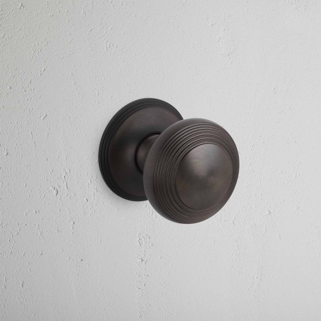 Bronze Poplar Passage Door Knob Set with subtle ridged detailing, shown installed on a white door.