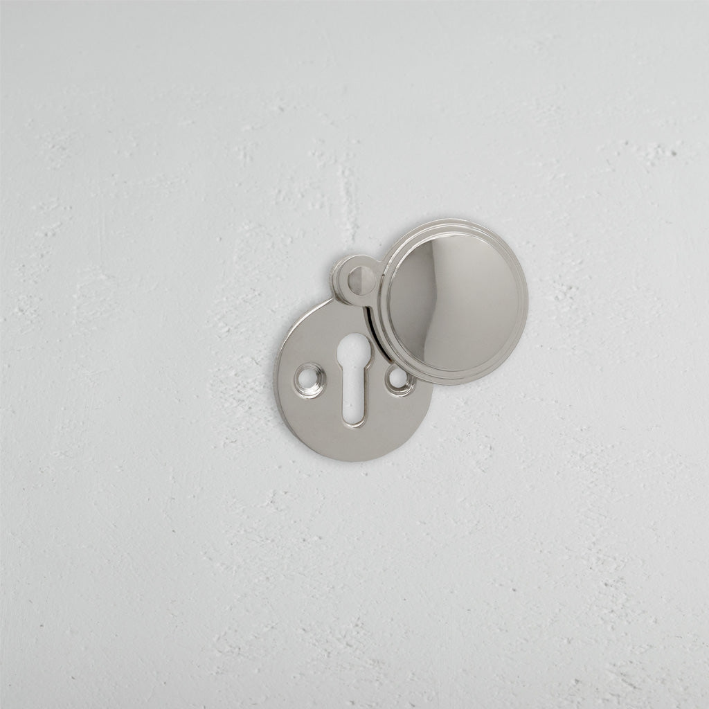 Warwick Covered Key Escutcheon in polished nickel with a round cover, partially open to show the keyhole.