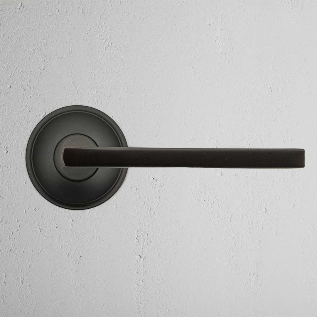 Clayton Dummy Door Handle Set in bronze finish with a round base, mounted on a white textured wall.