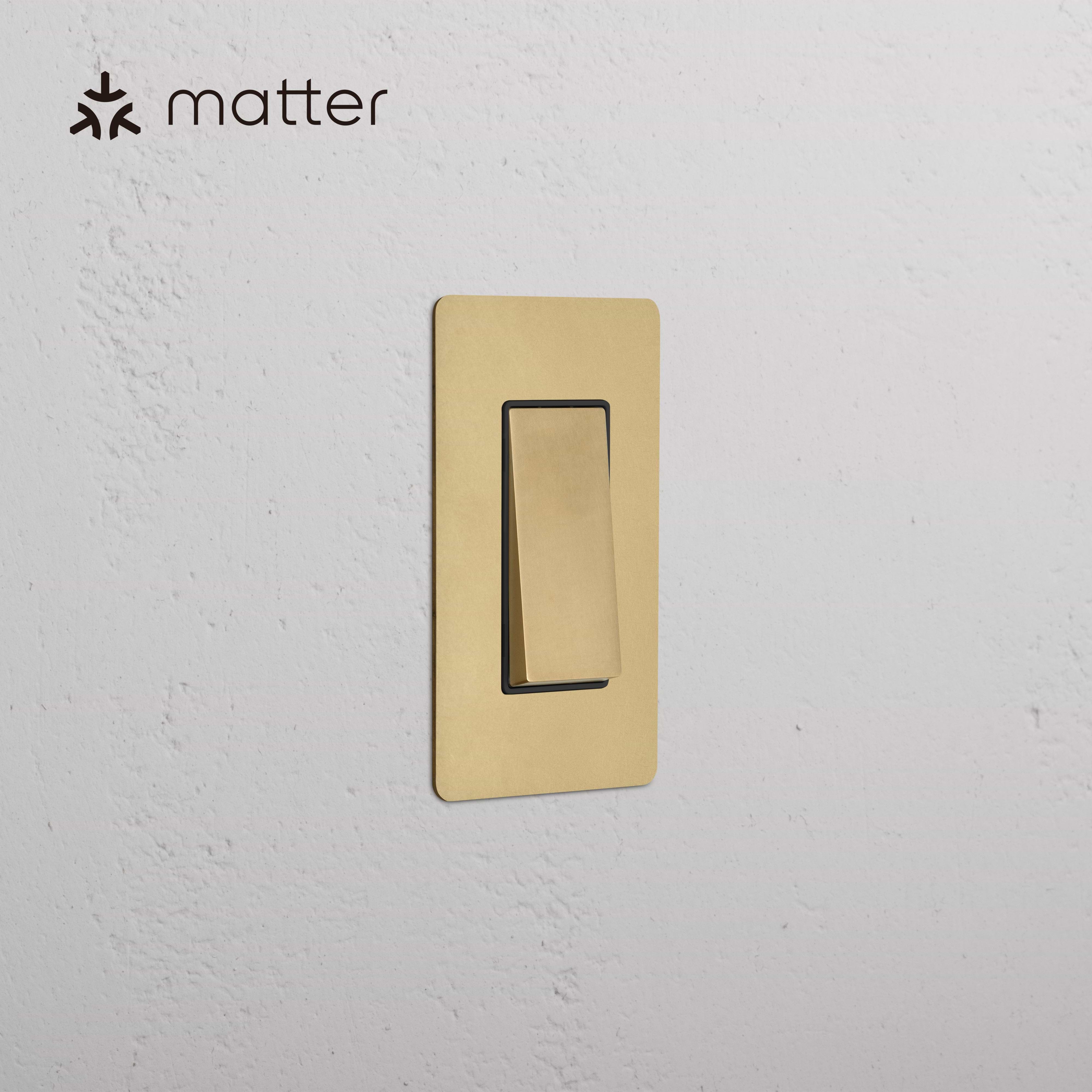 Kew 1G Smart Retractive Rocker Switch in Antique Brass Black, shown mounted on a textured white wall.