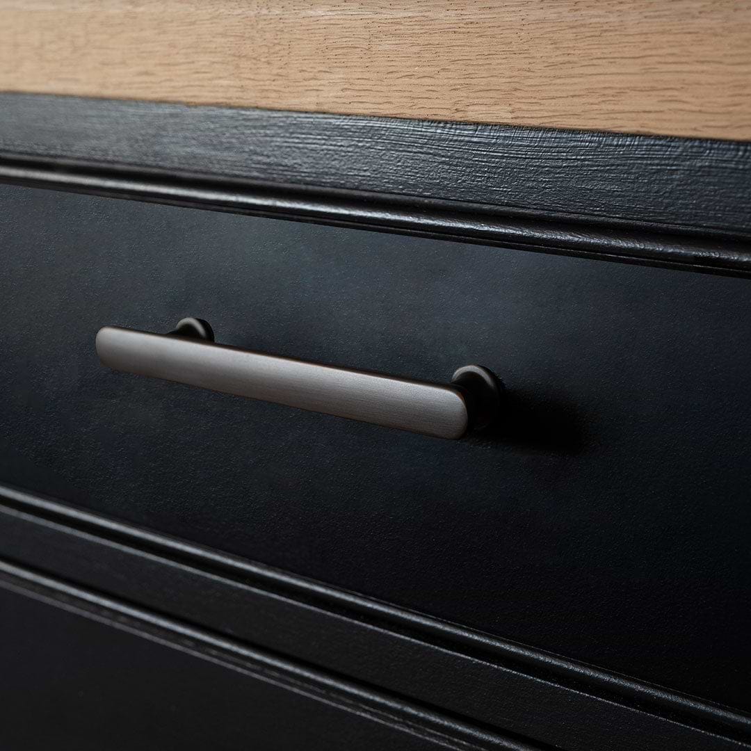 Close-up of a small bronze Milliner furniture handle mounted on a black drawer below a wooden countertop.