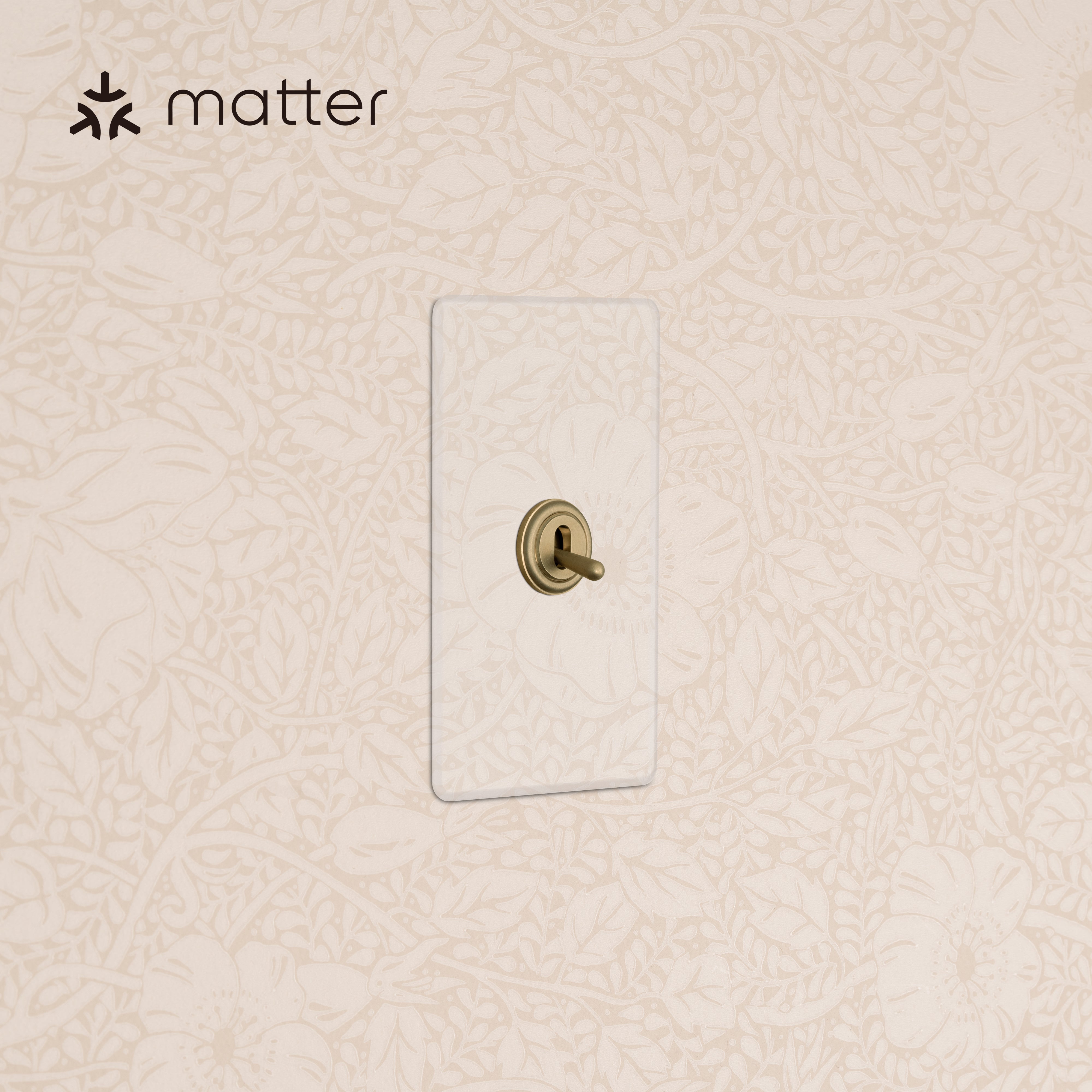 Kew 1G Smart Retractive Toggle Switch in Clear Antique Brass with clear faceplate on a cream floral wall.