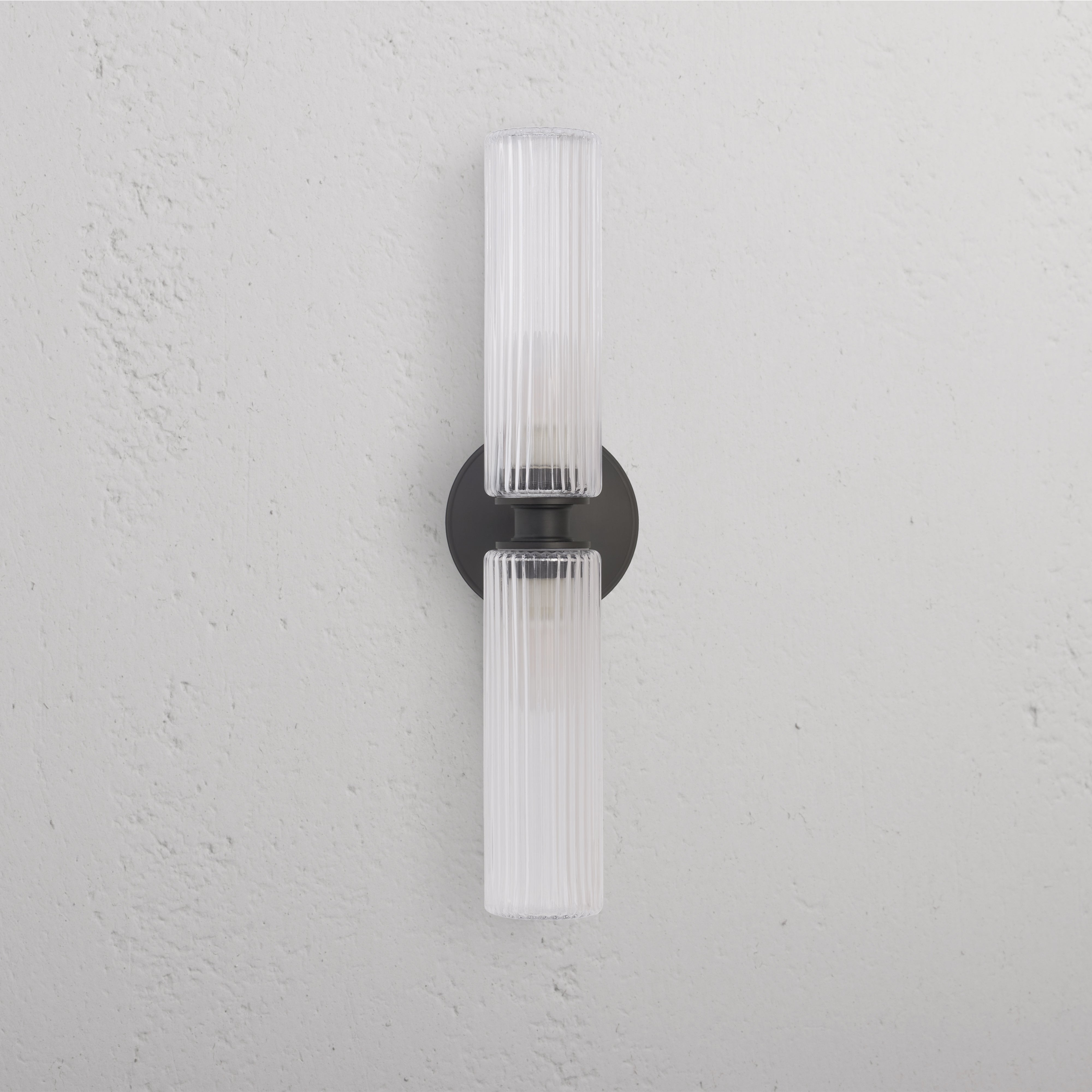 Claremont Medium Wall Light with fluted glass and bronze round base, mounted on a white wall.