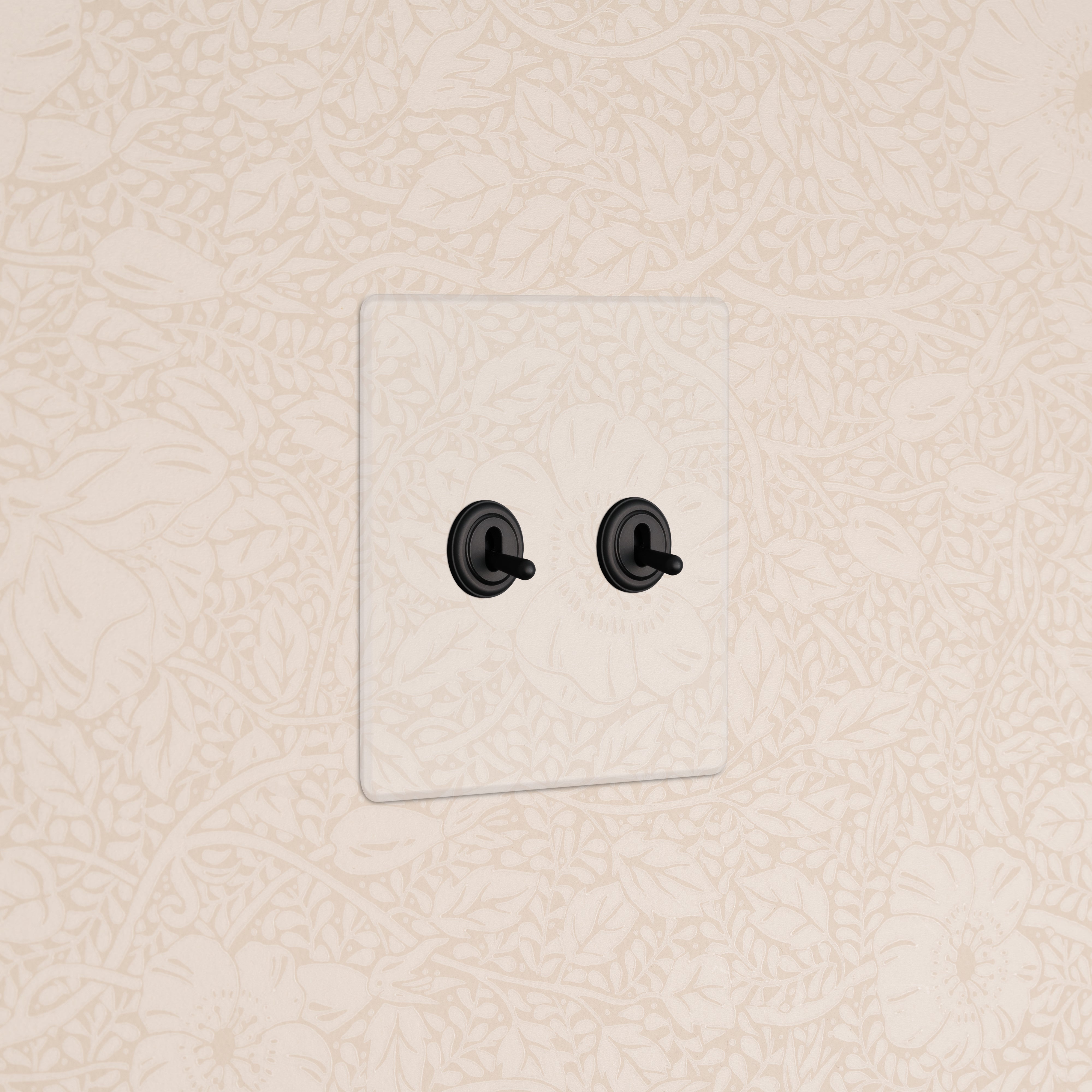 Kew 2G Toggle Switch - Clear Bronze with two black toggles installed on beige floral-patterned wallpaper.