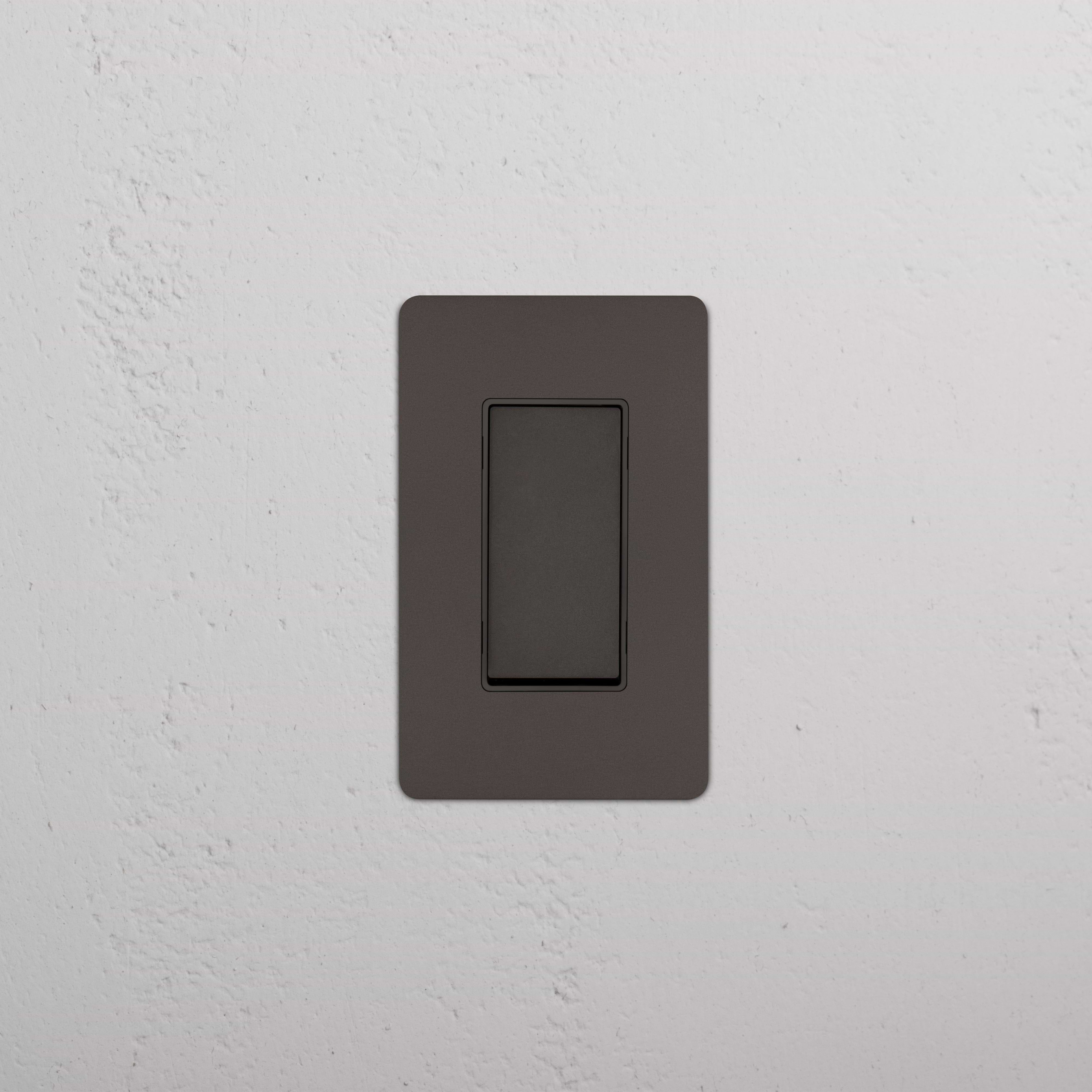 Kew 1G Retractive Rocker Switch in Bronze Black with matching wall plate, installed on a white wall.