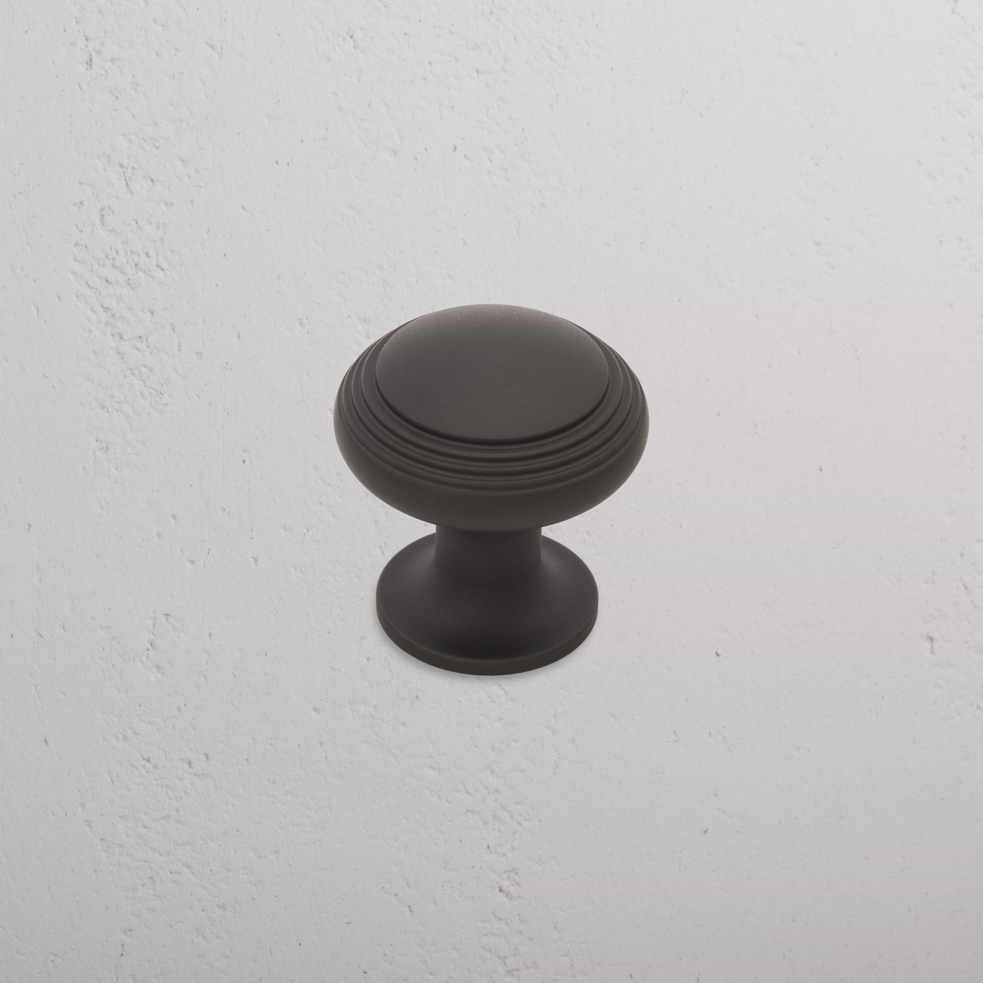 Medium-sized round bronze Barlow furniture knob with ridged detailing, shown on a textured white surface.