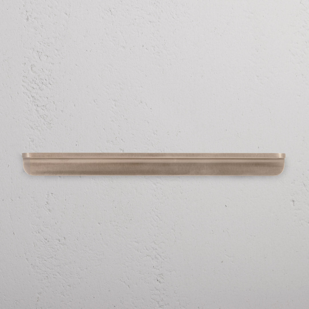 Oxford Furniture Handle Medium in antique brass with a minimalist, rounded design, mounted on a white surface.