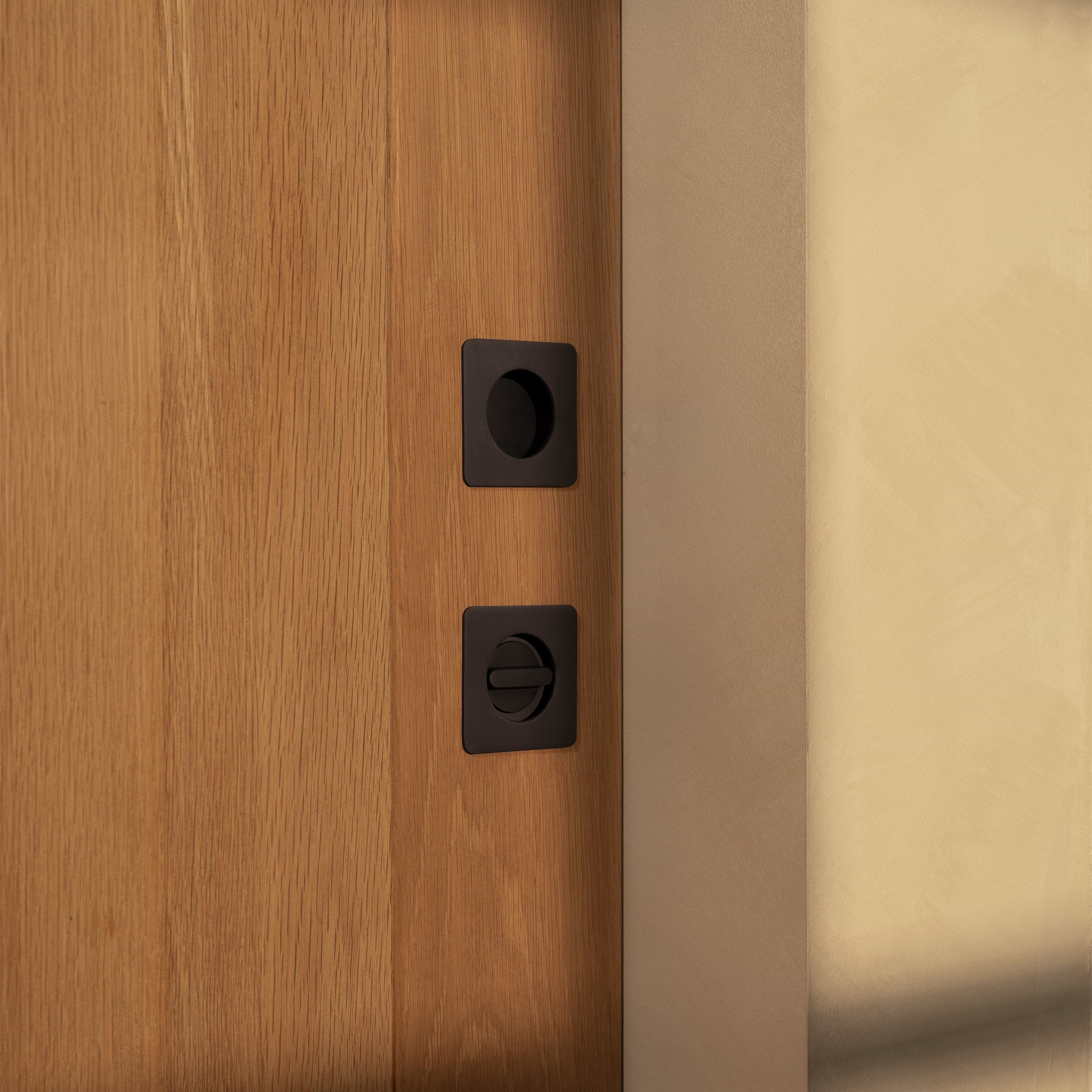 Bronze Regent Recessed Thumbturn installed on a wooden door, shown in close-up against a neutral wall.