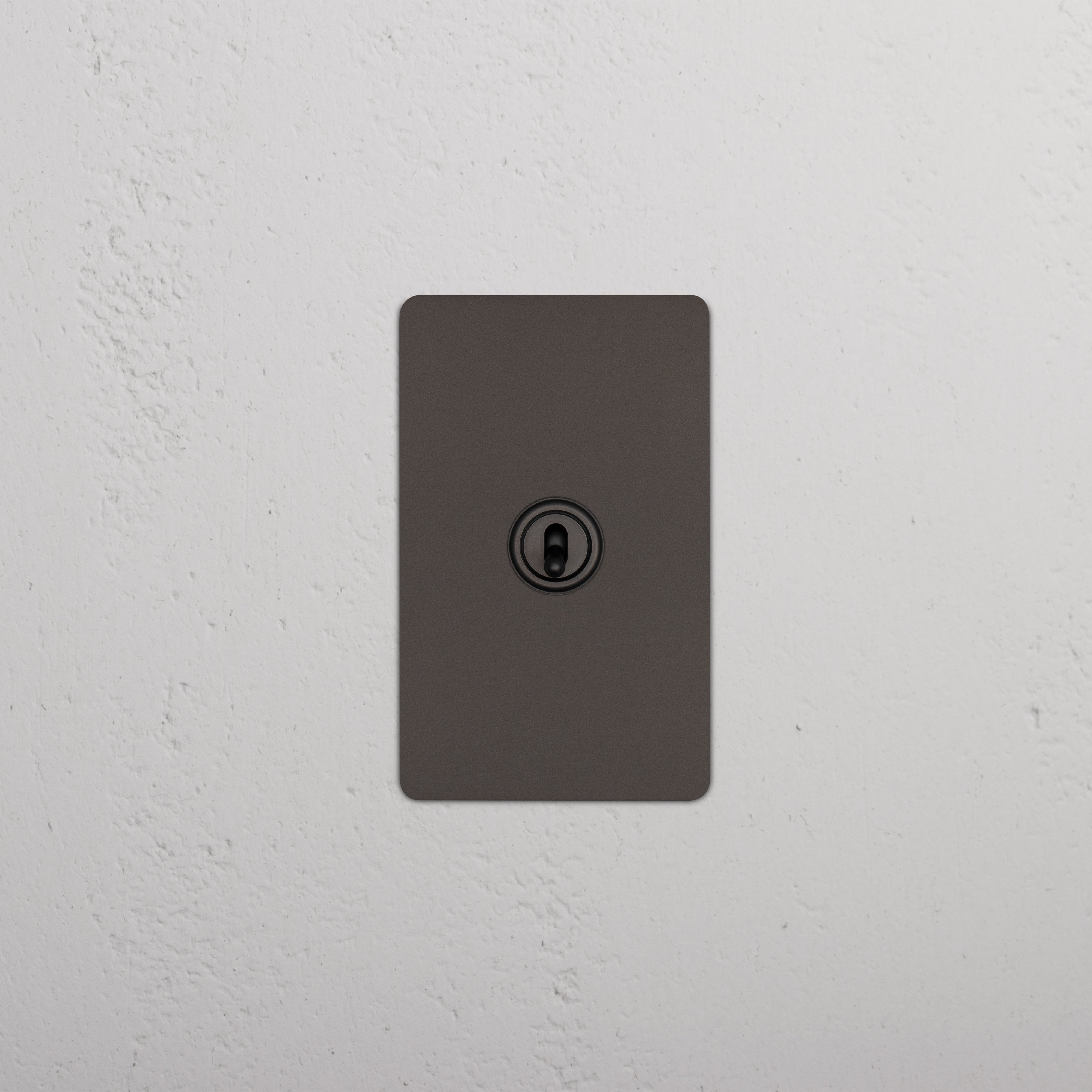 Bronze Kew 1G Retractive Toggle Switch with central toggle, mounted on a white textured wall.