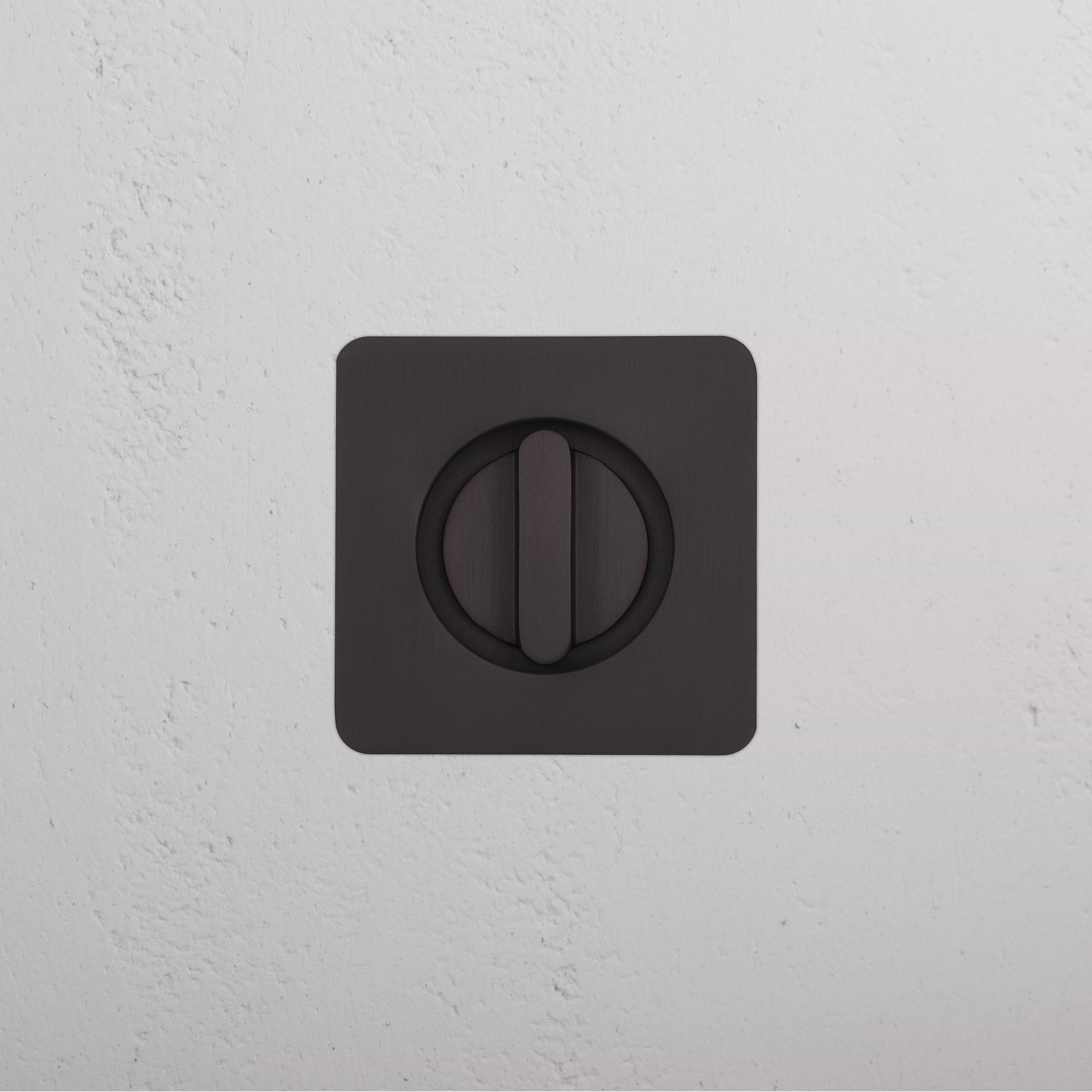 Bronze Regent Recessed Thumbturn with central rotating knob, mounted on a textured white wall.