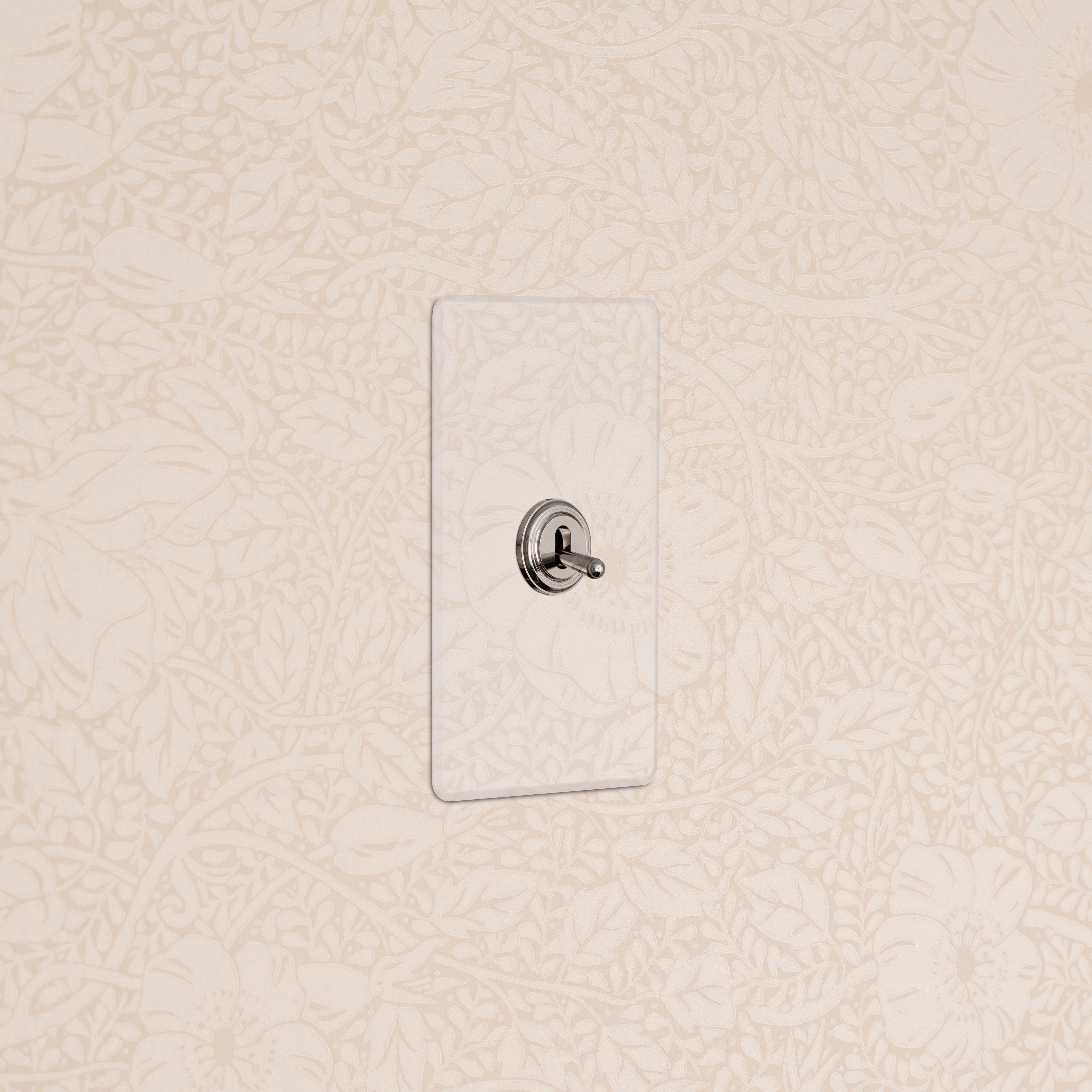 Kew 1G Toggle Switch in Clear Polished Nickel mounted on a wall with cream floral wallpaper.