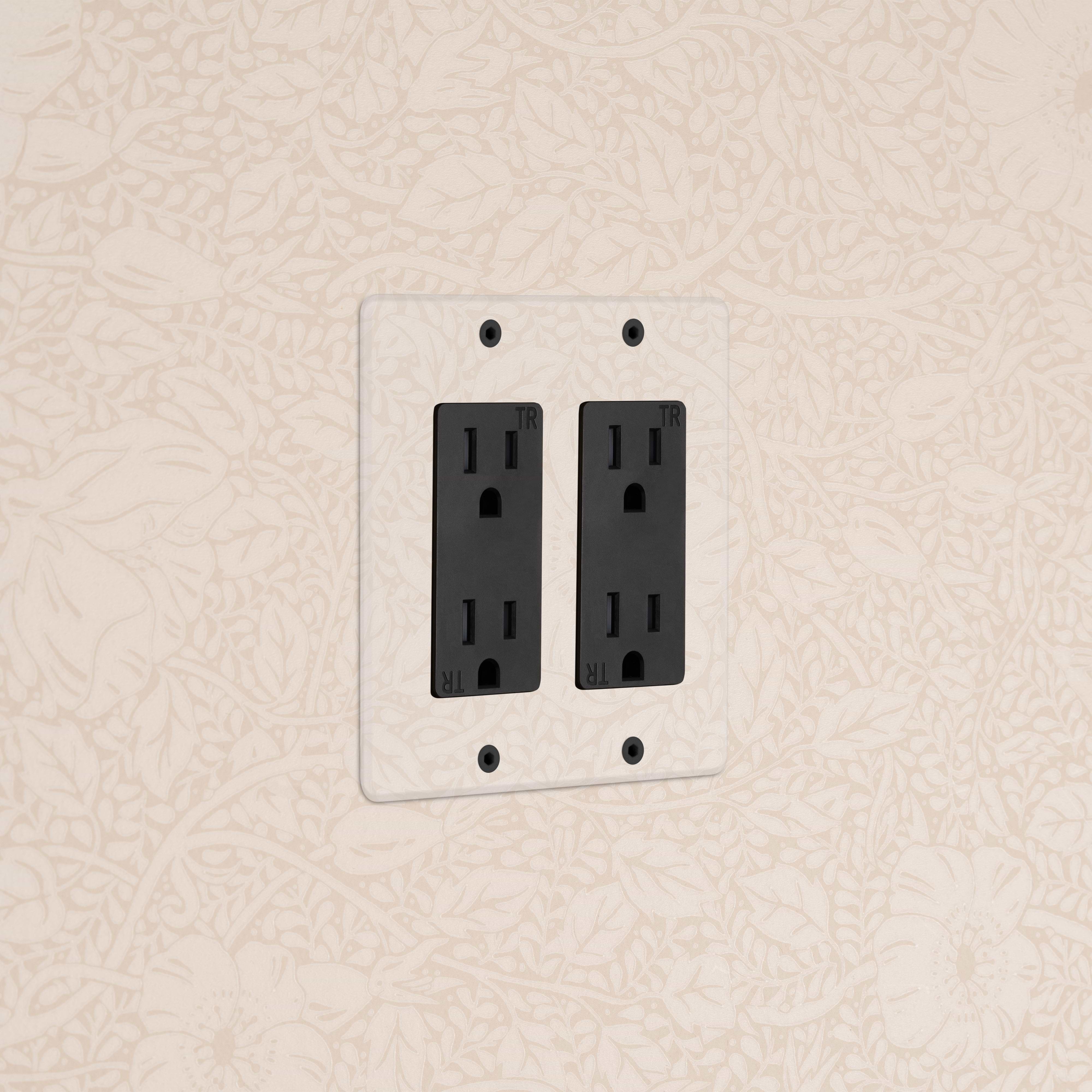 Kew 2G Outlet in Clear Black, double electrical socket on a wall with floral-patterned wallpaper.