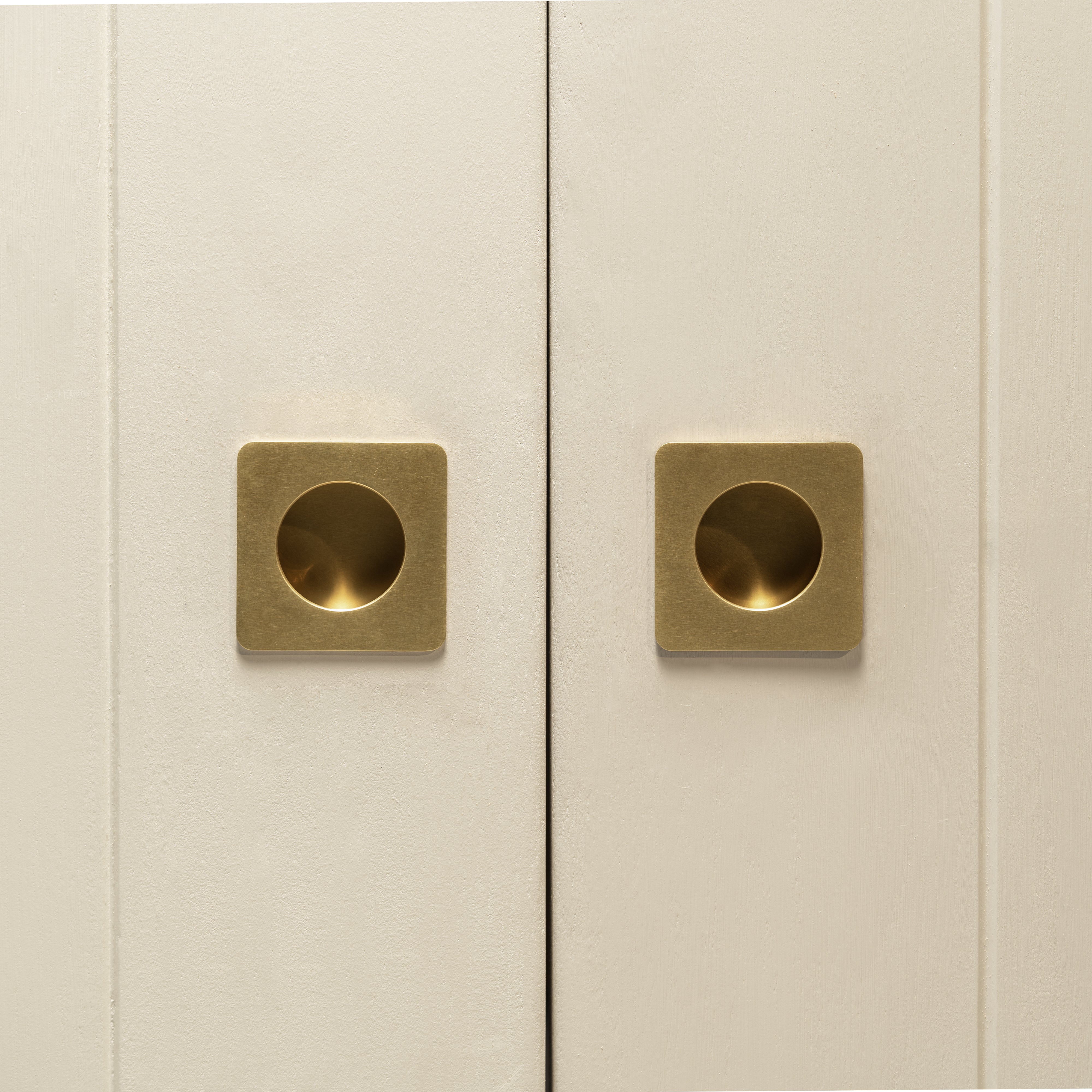 Close-up of two cabinet doors with Regent Recessed Small Pulls in Antique Brass, center-mounted and minimalistic.