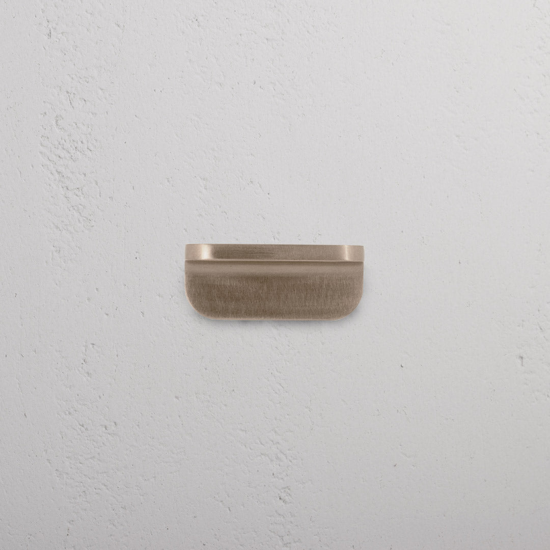 Oxford Furniture Handle Extra Small in Antique Brass, rectangular pull handle on a white textured surface.