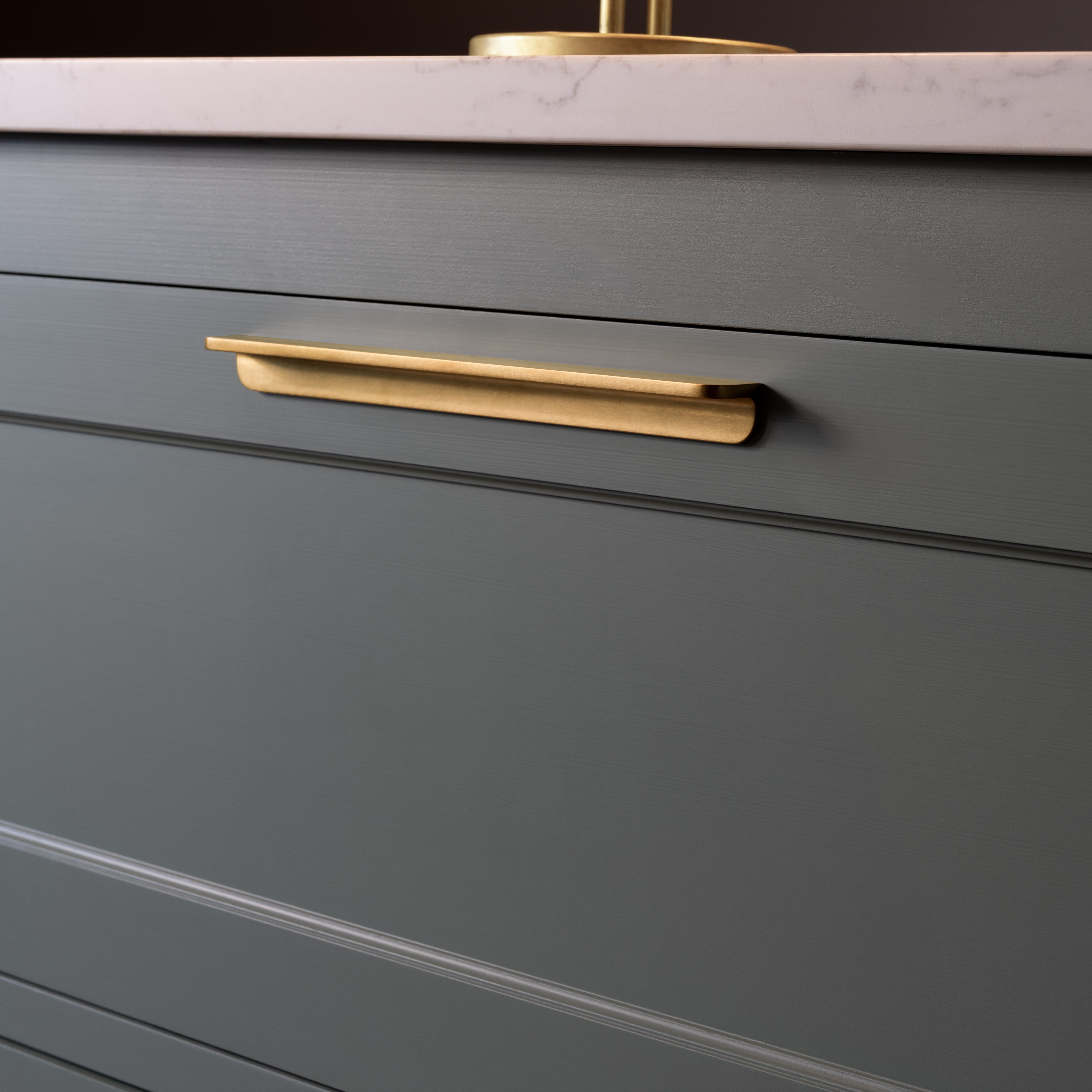 Medium-sized Oxford Furniture Handle in antique brass fitted to a green cabinet drawer under a marble countertop.