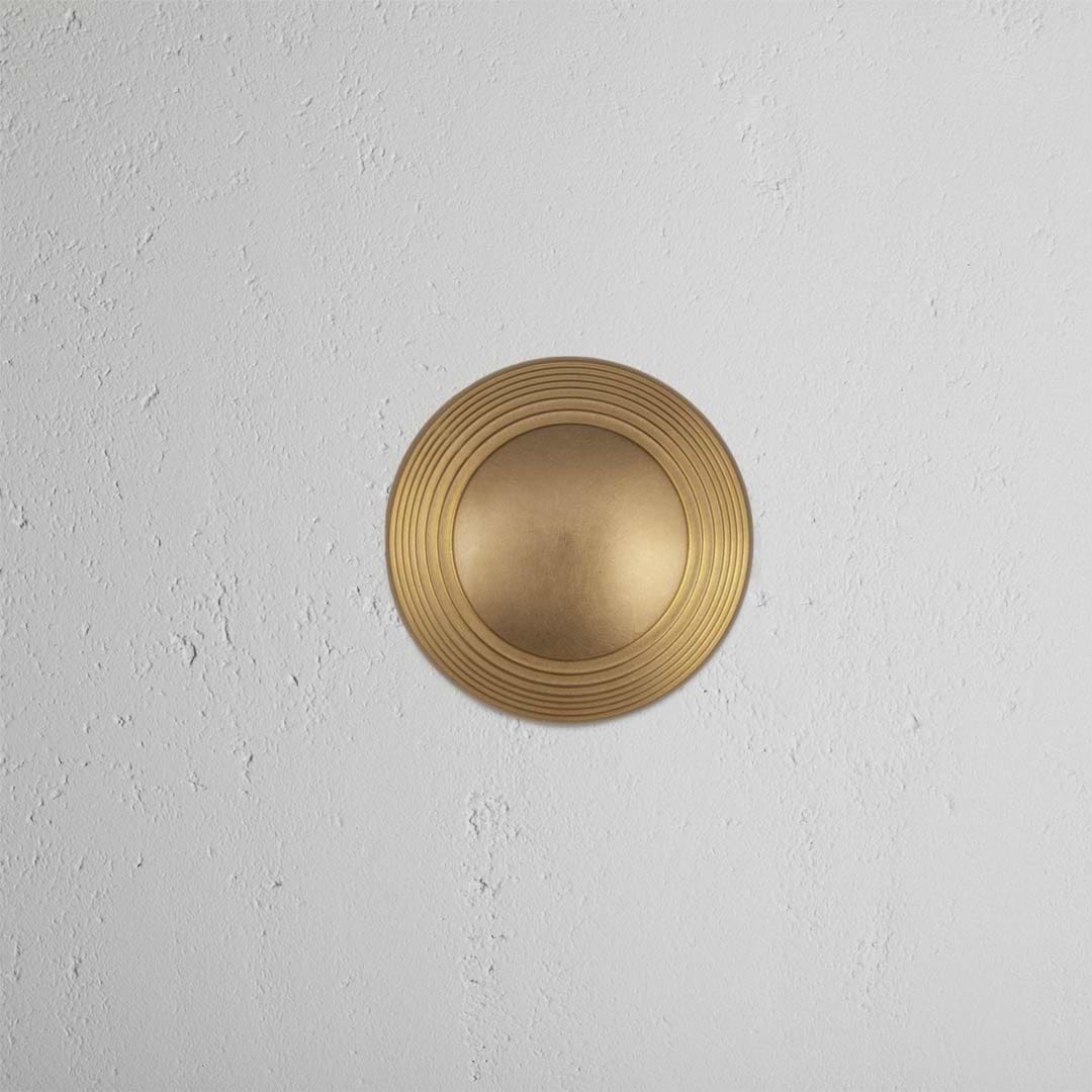 Poplar Passage Door Knob Set in antique brass finish, featuring concentric ring details, on a white wall.