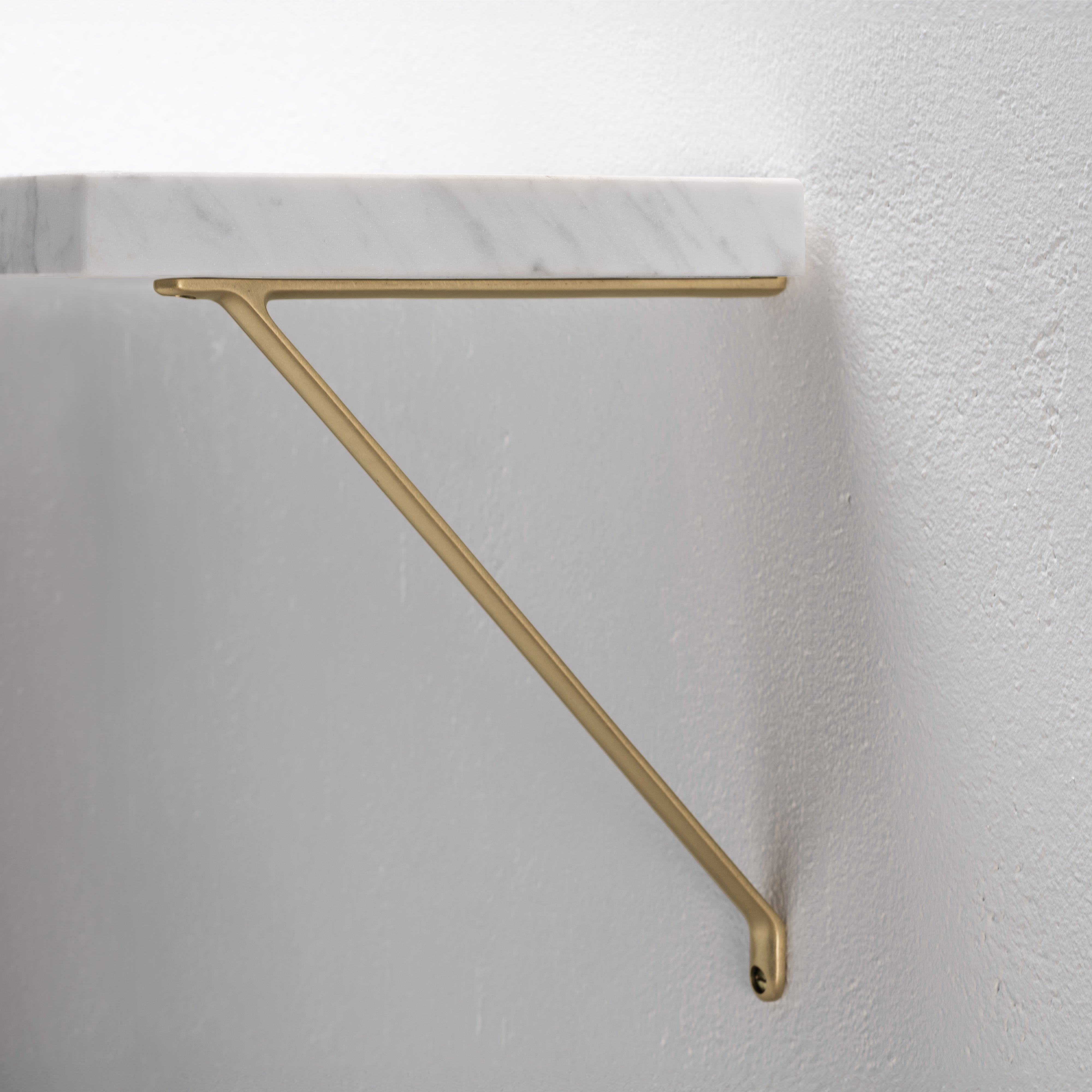 Medium-sized Brixton Shelf Bracket in antique brass, mounted on a white wall and supporting a shelf.