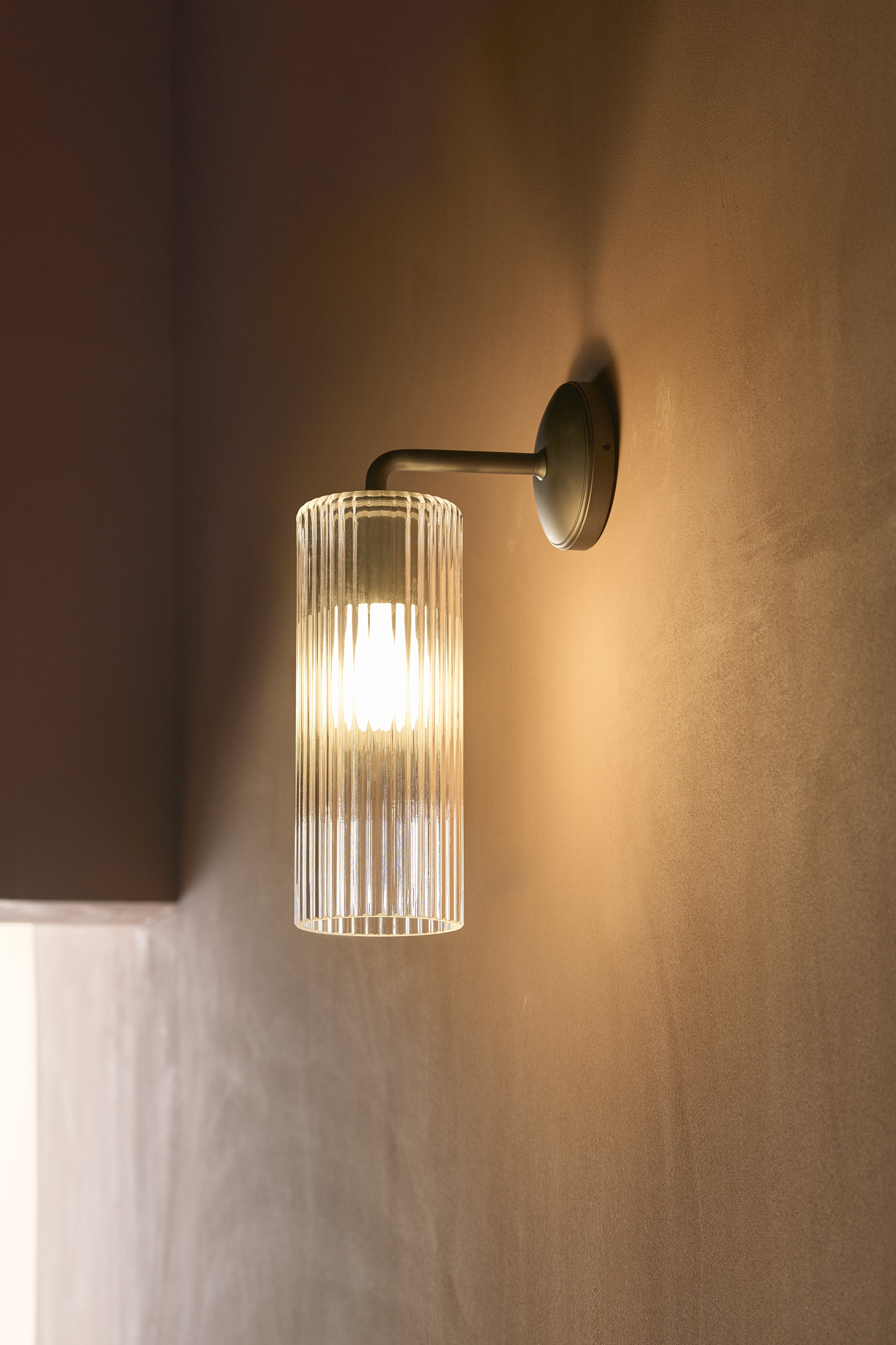Large Claremont Wall Light with fluted glass in bronze finish, mounted on a wall and illuminated.