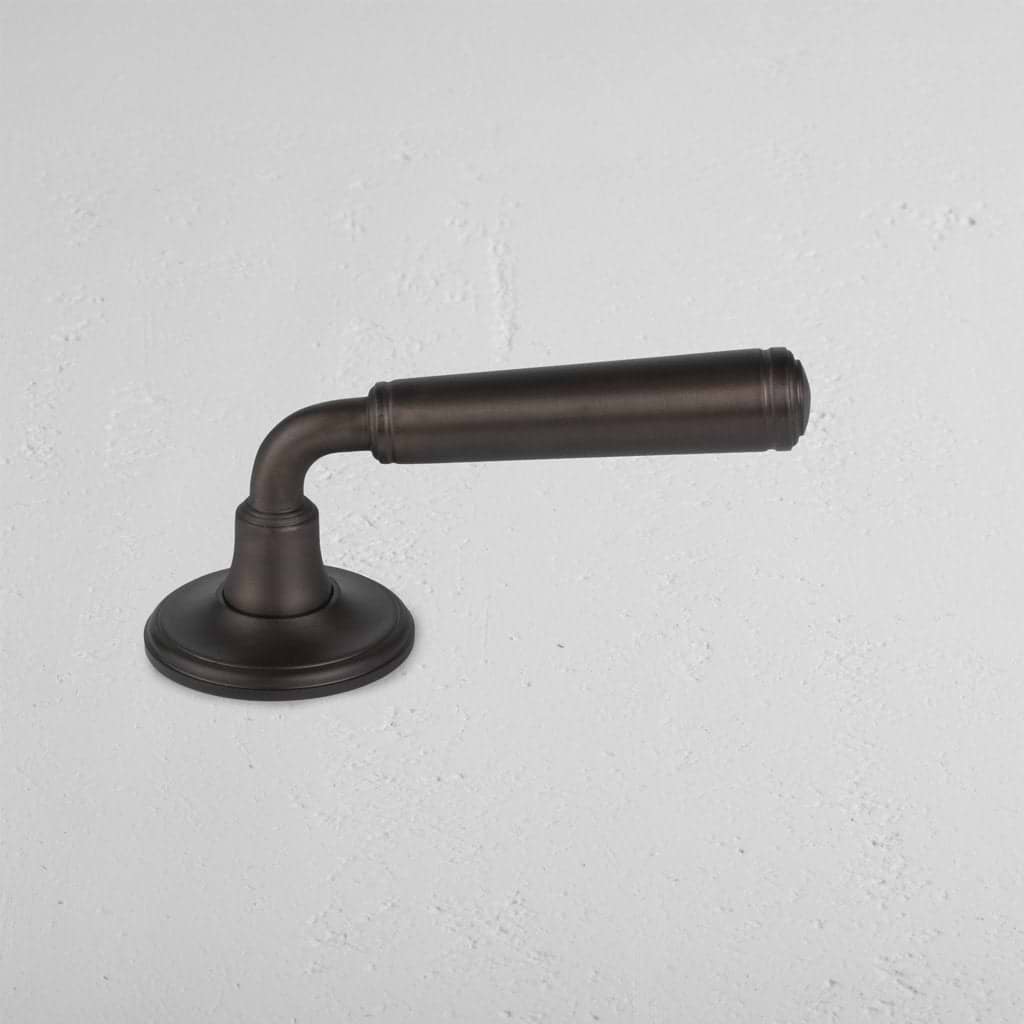 Digby Passage Door Handle Unsprung in bronze with a round base and cylindrical lever, on a light surface.