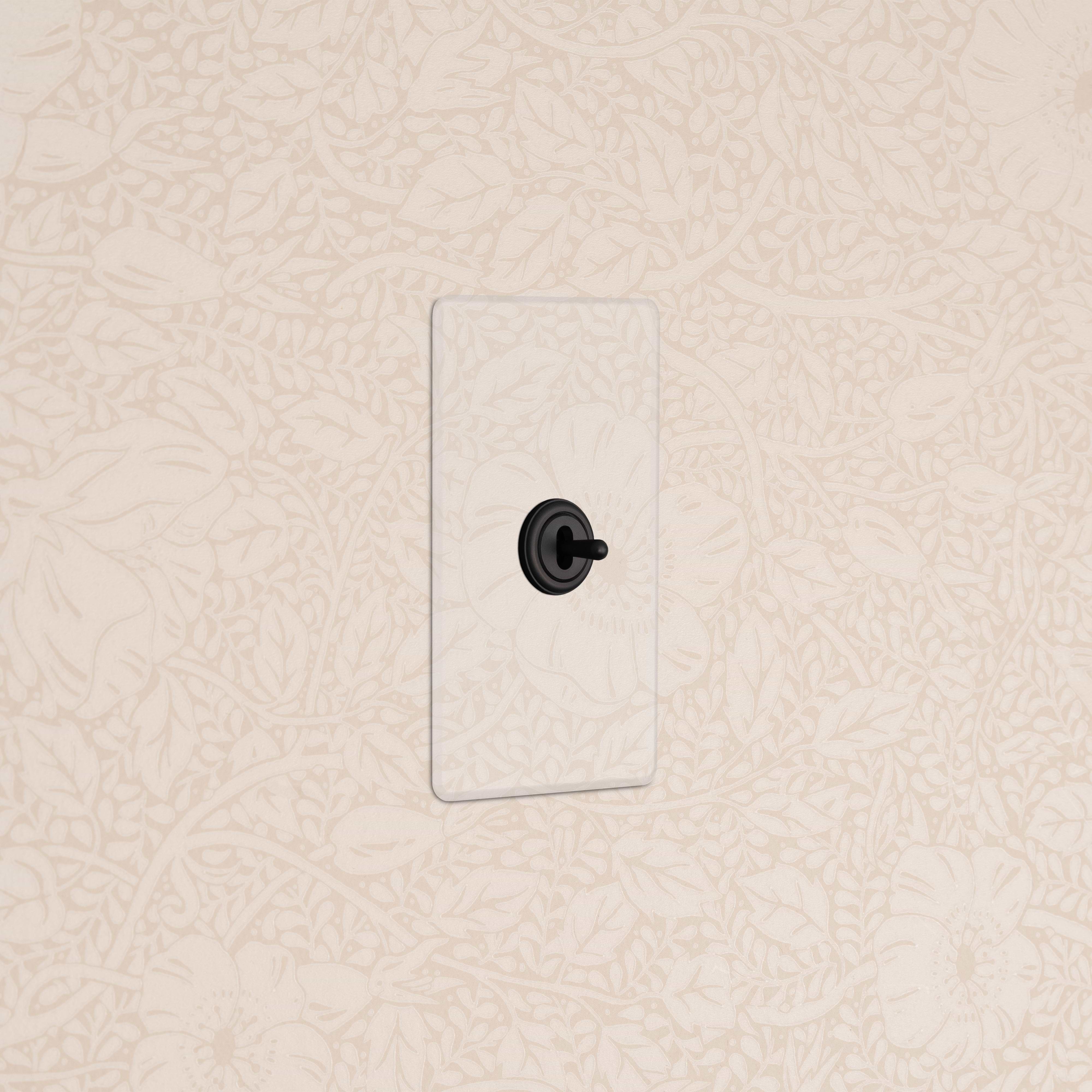 Kew 1G Center Retractive Toggle Switch in clear bronze mounted on wall with cream floral wallpaper.