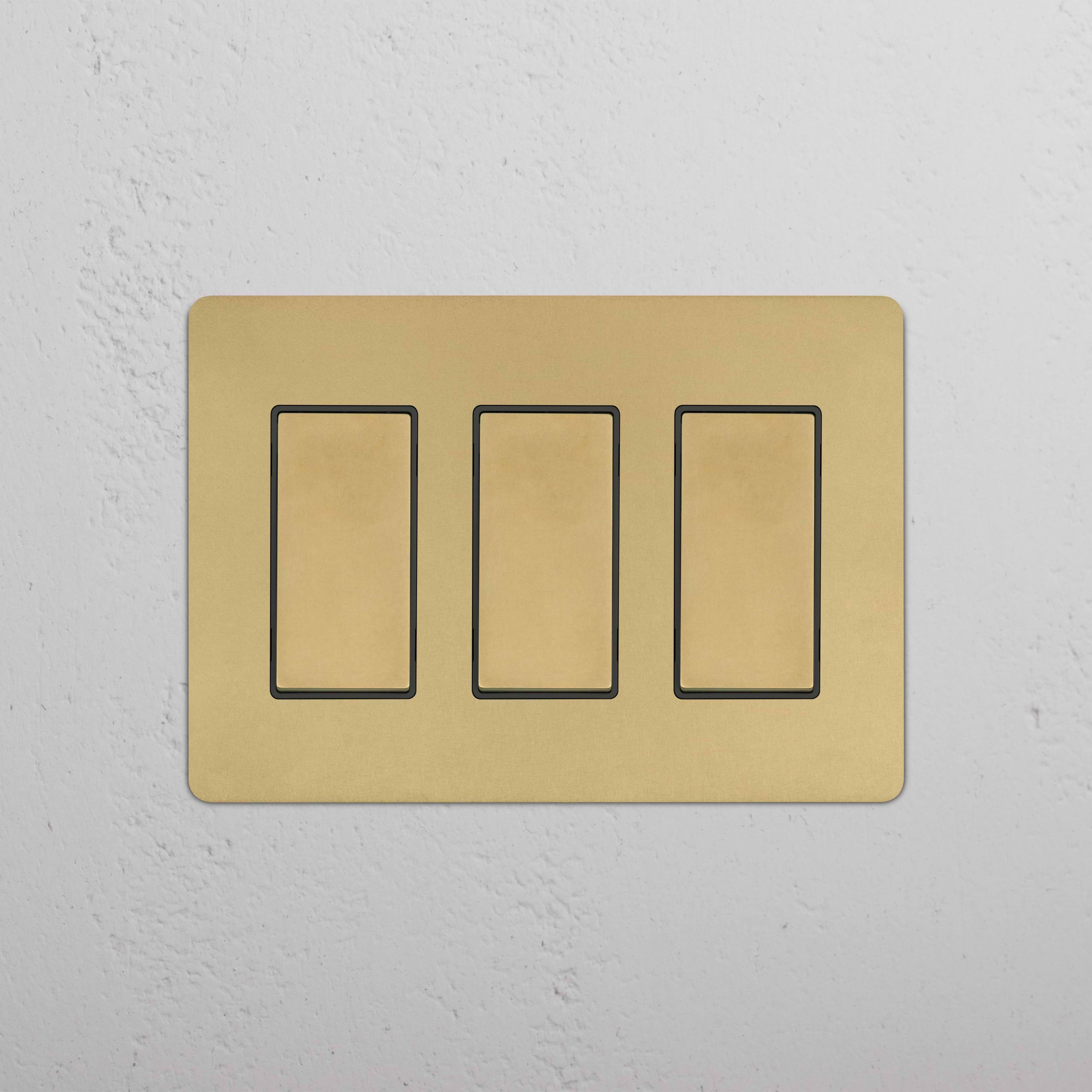 Kew 3G Rocker Switch in Antique Brass Black with three black rectangular switches on a gold-finish plate.