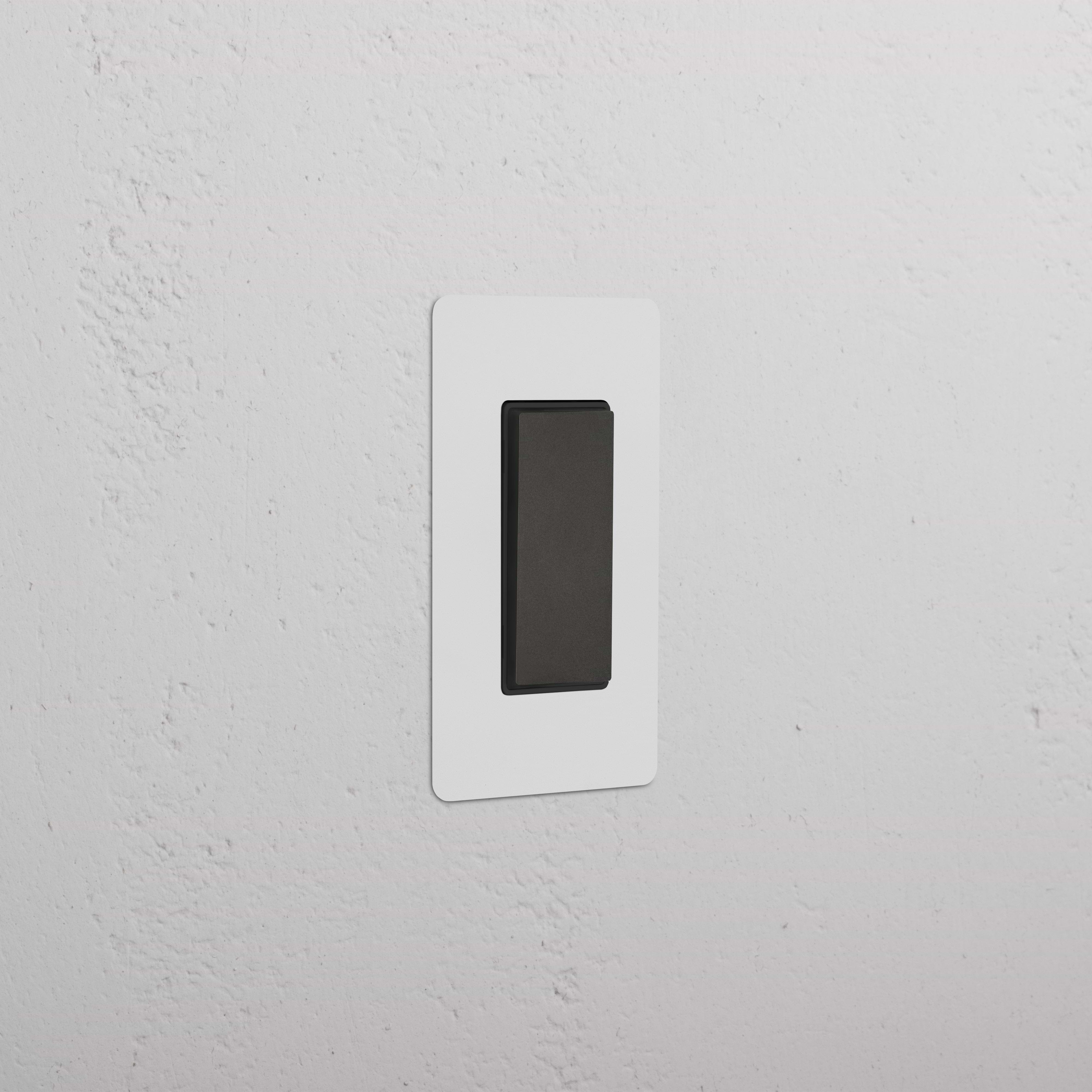 Kew 1G Center Retractive Rocker Switch in Paintable Bronze Black, shown installed on a white wall.