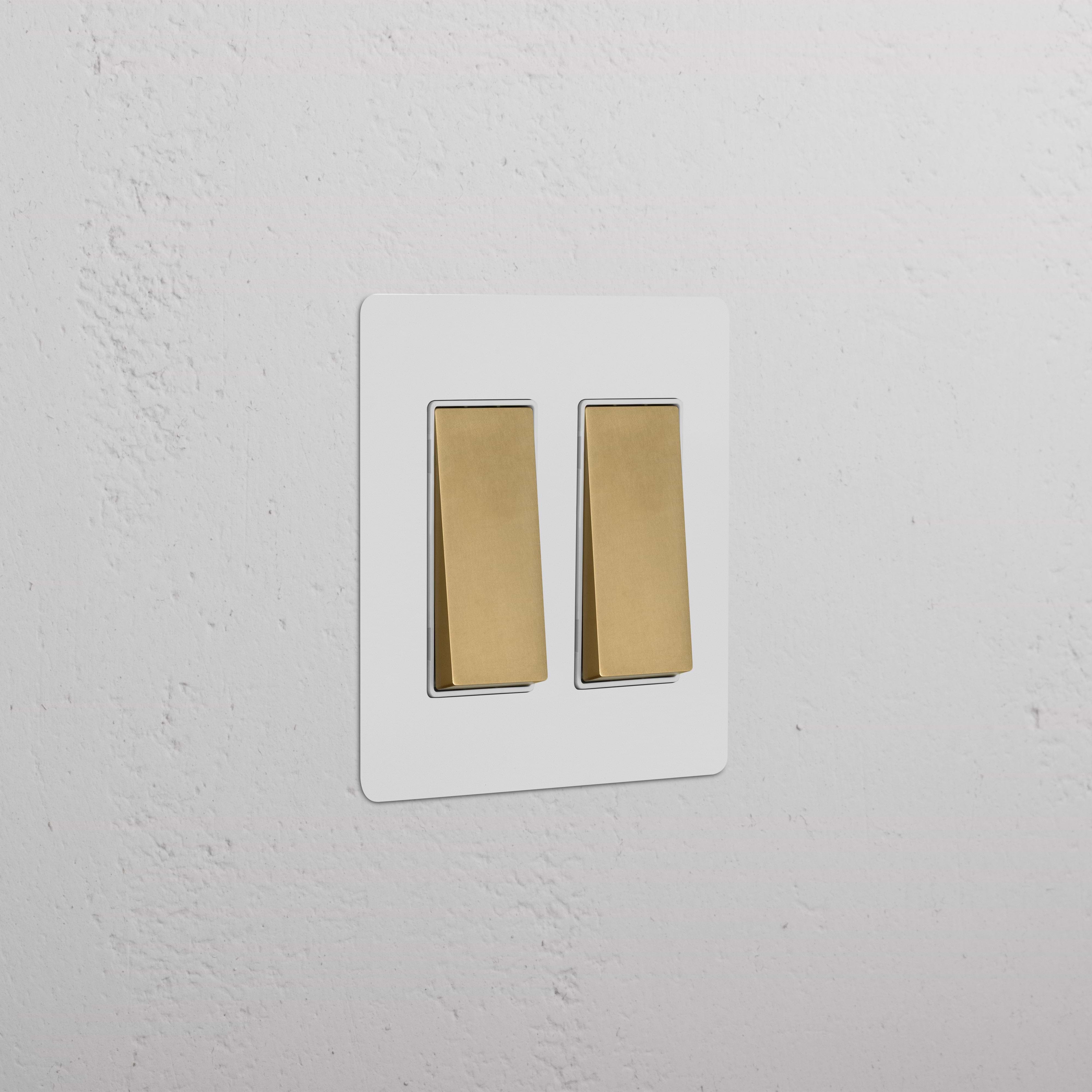 Kew 2G Rocker Switch in paintable antique brass white finish on a rectangular plate against a white wall.