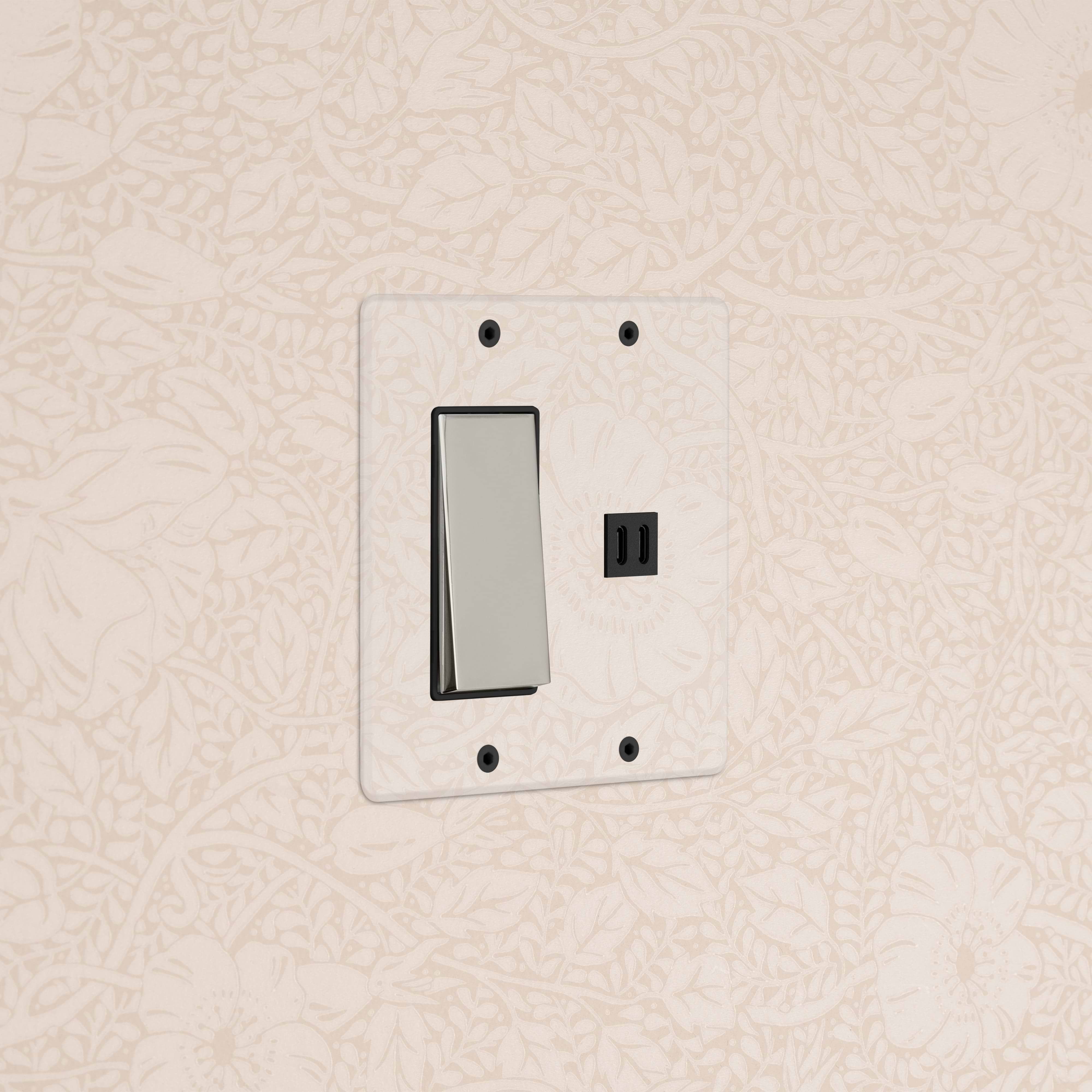 Clear polished nickel black Kew 2G rocker switch with fast charge USB on a wall against beige floral wallpaper.