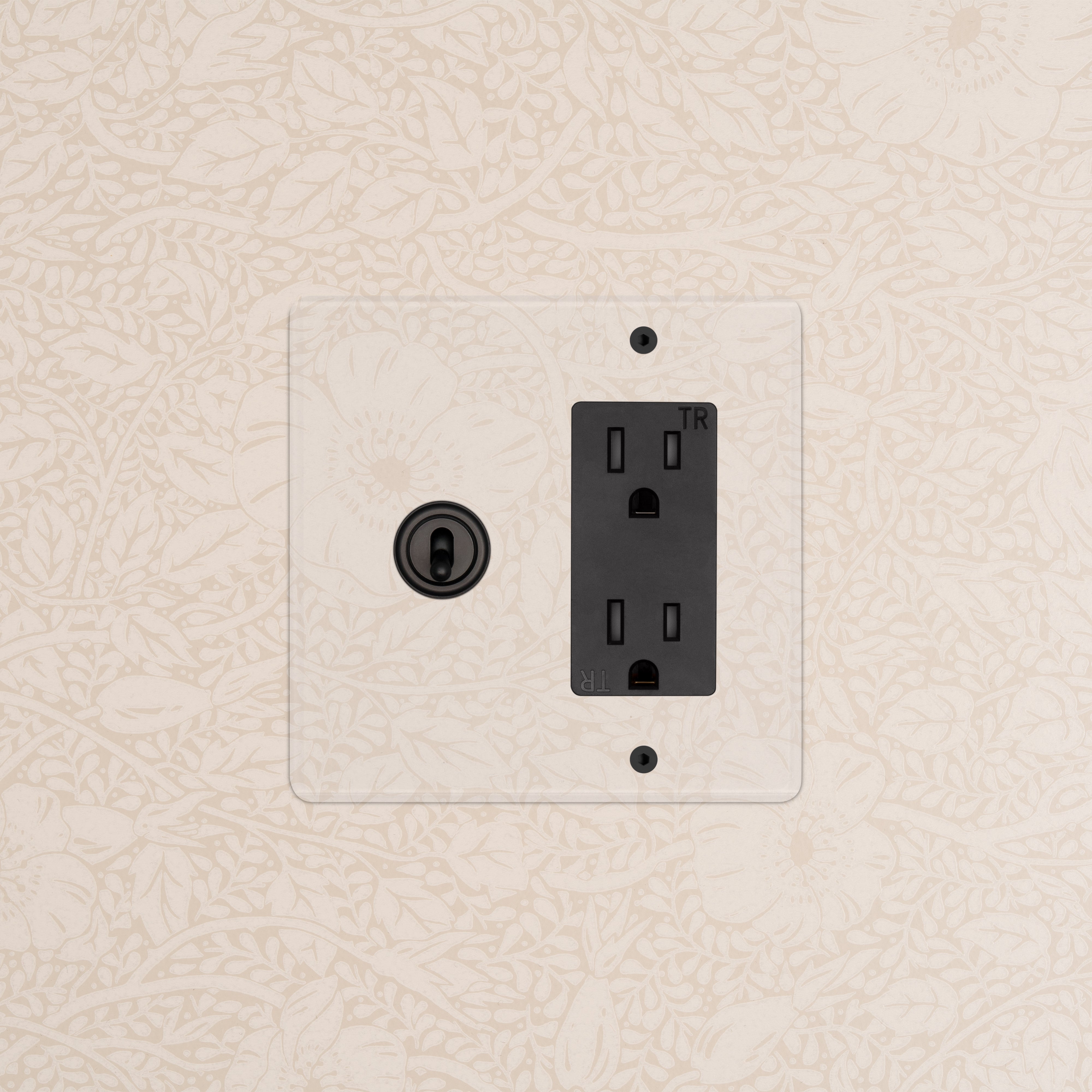 Kew 2G Toggle Switch & Outlet in Clear Bronze Black finish mounted on a wall with subtle floral pattern.