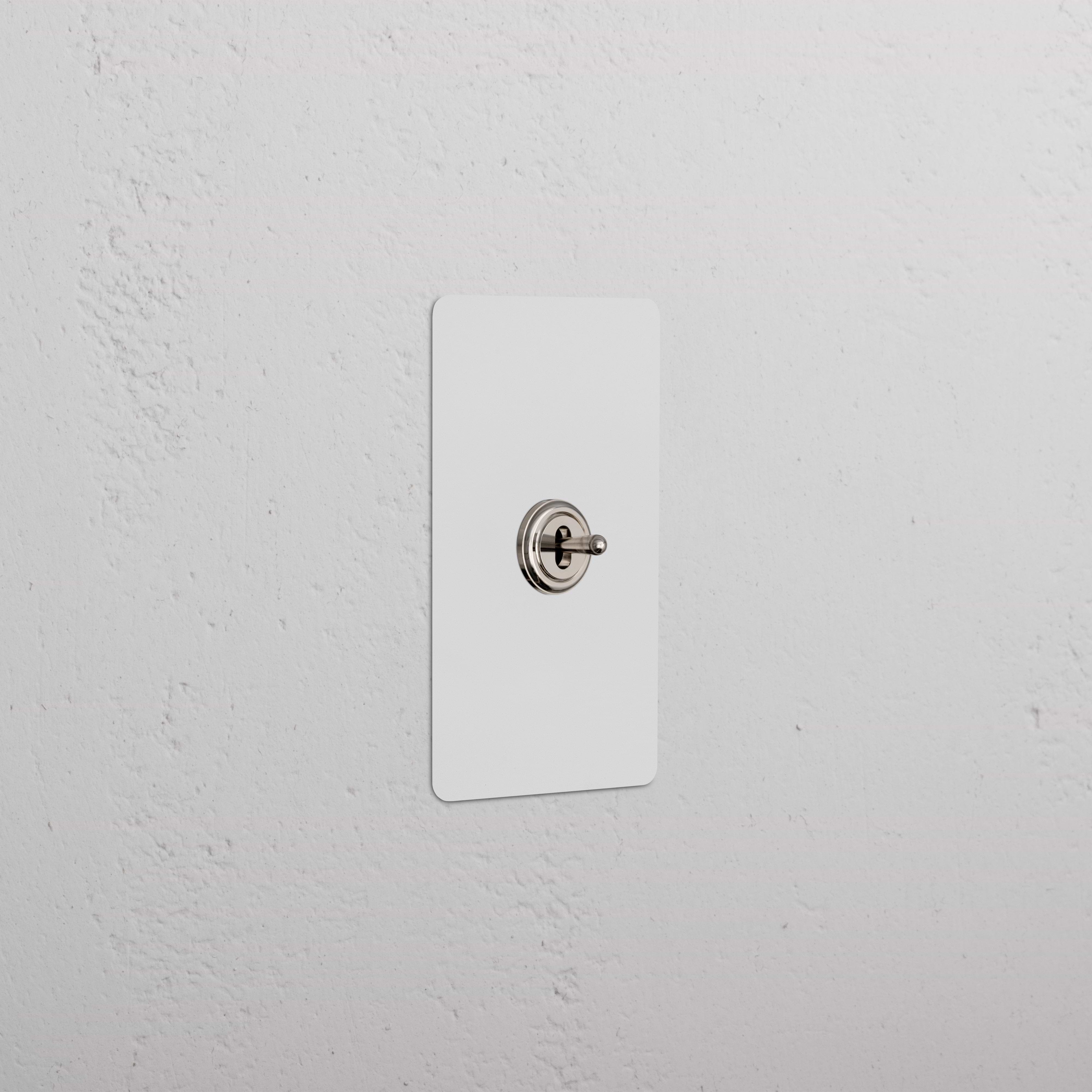 Kew 1G Center Retractive Toggle Switch in paintable polished nickel, mounted on a white textured wall.