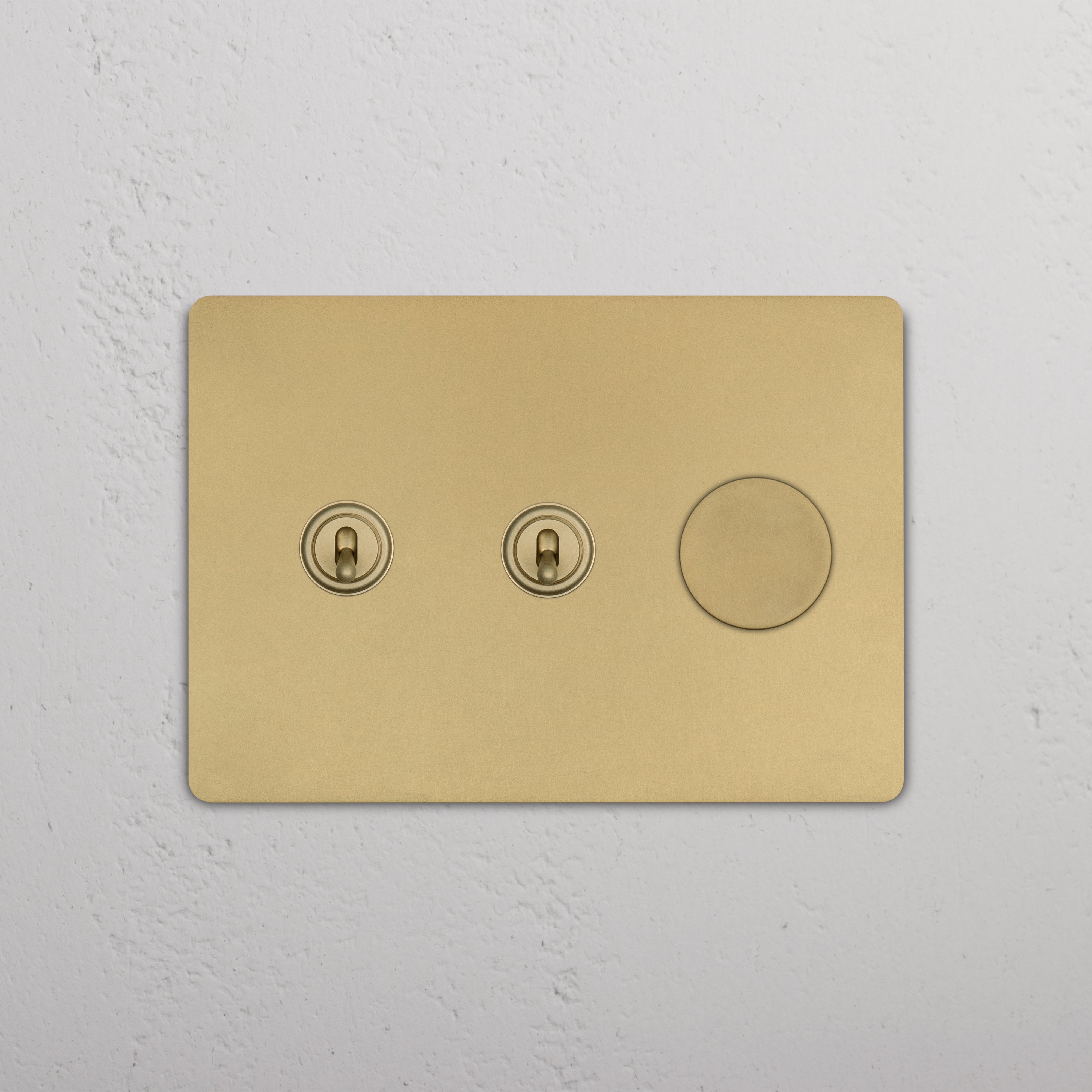Grove 3G antique brass switch with two toggles and one dimmer, mounted on a textured white wall.