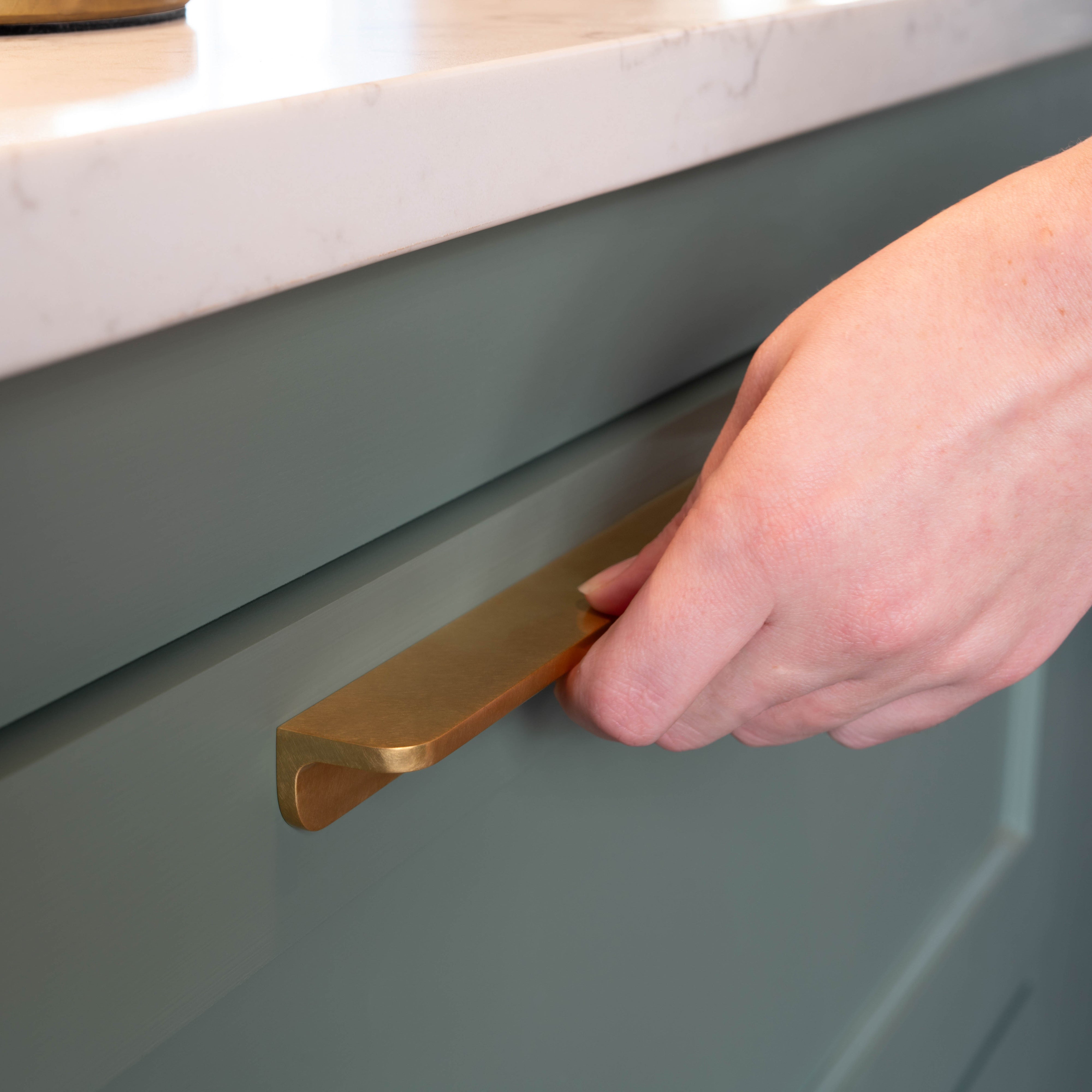 A medium-sized Oxford Furniture Handle in antique brass fitted to a green cabinet drawer beneath a white countertop.