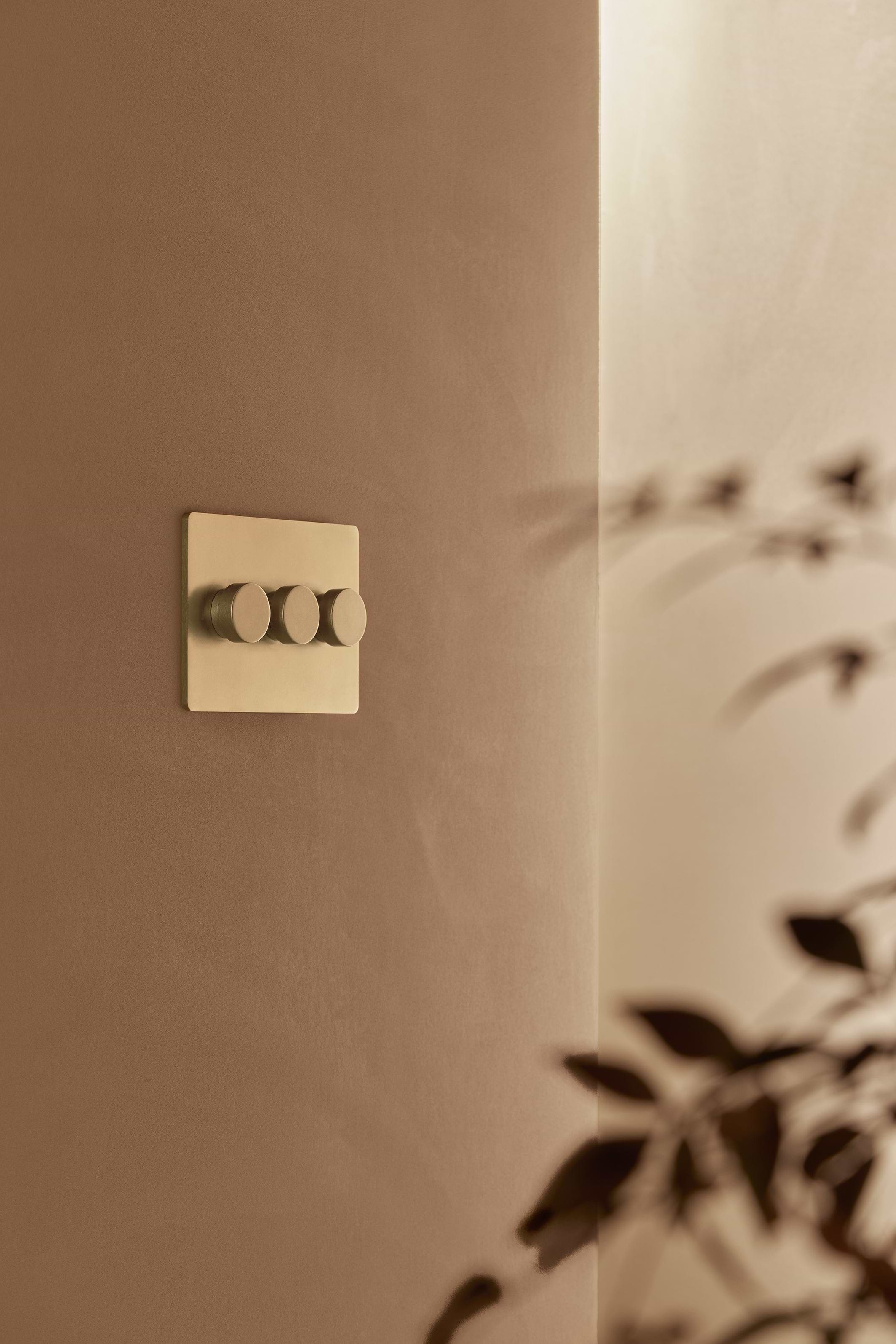 Grove 3G Dimmer Switch in Antique Brass featuring three round switches on a beige wall.