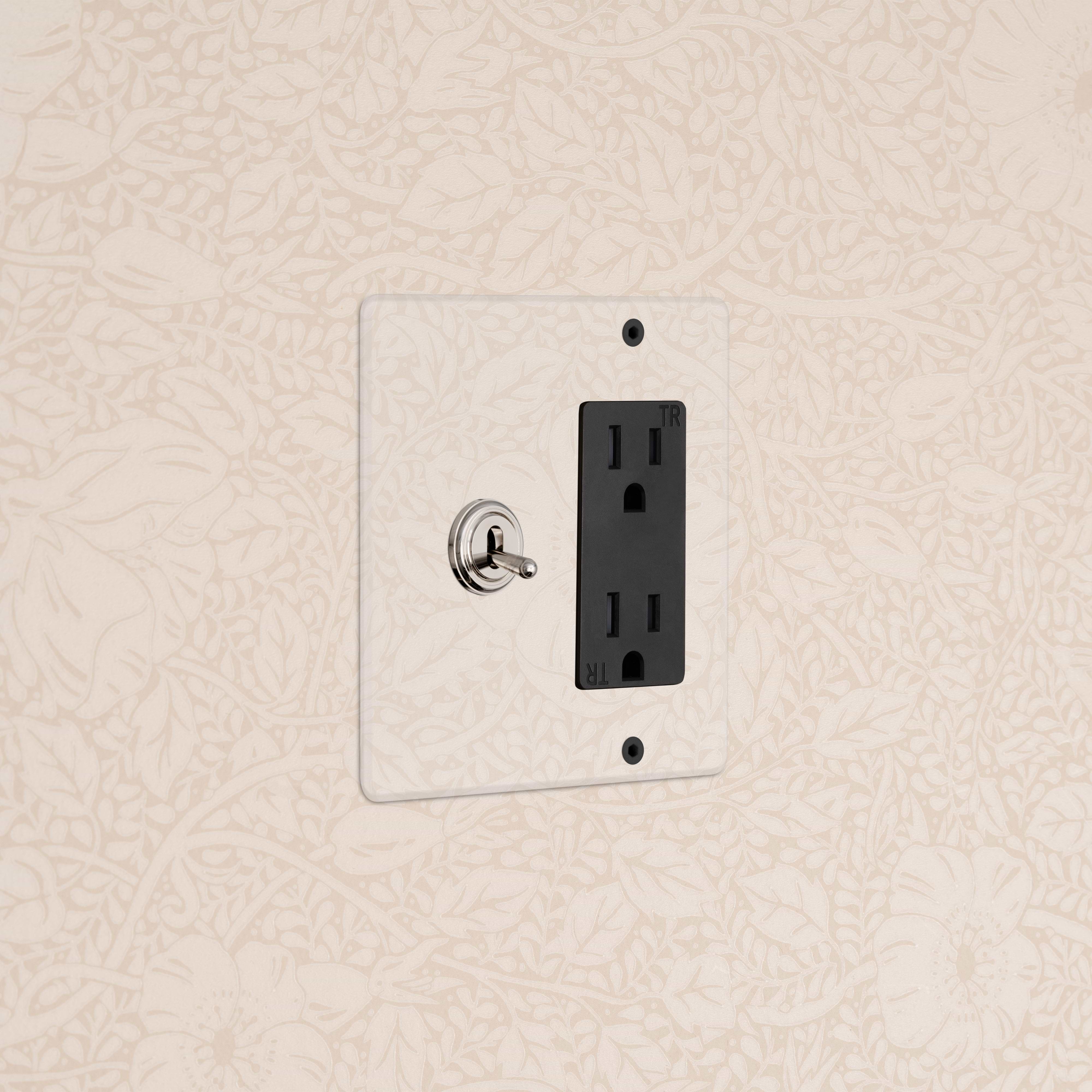 Kew 2G Toggle Switch & Outlet in Clear Polished Nickel Black on beige floral wallpaper; toggle and outlet visible.
