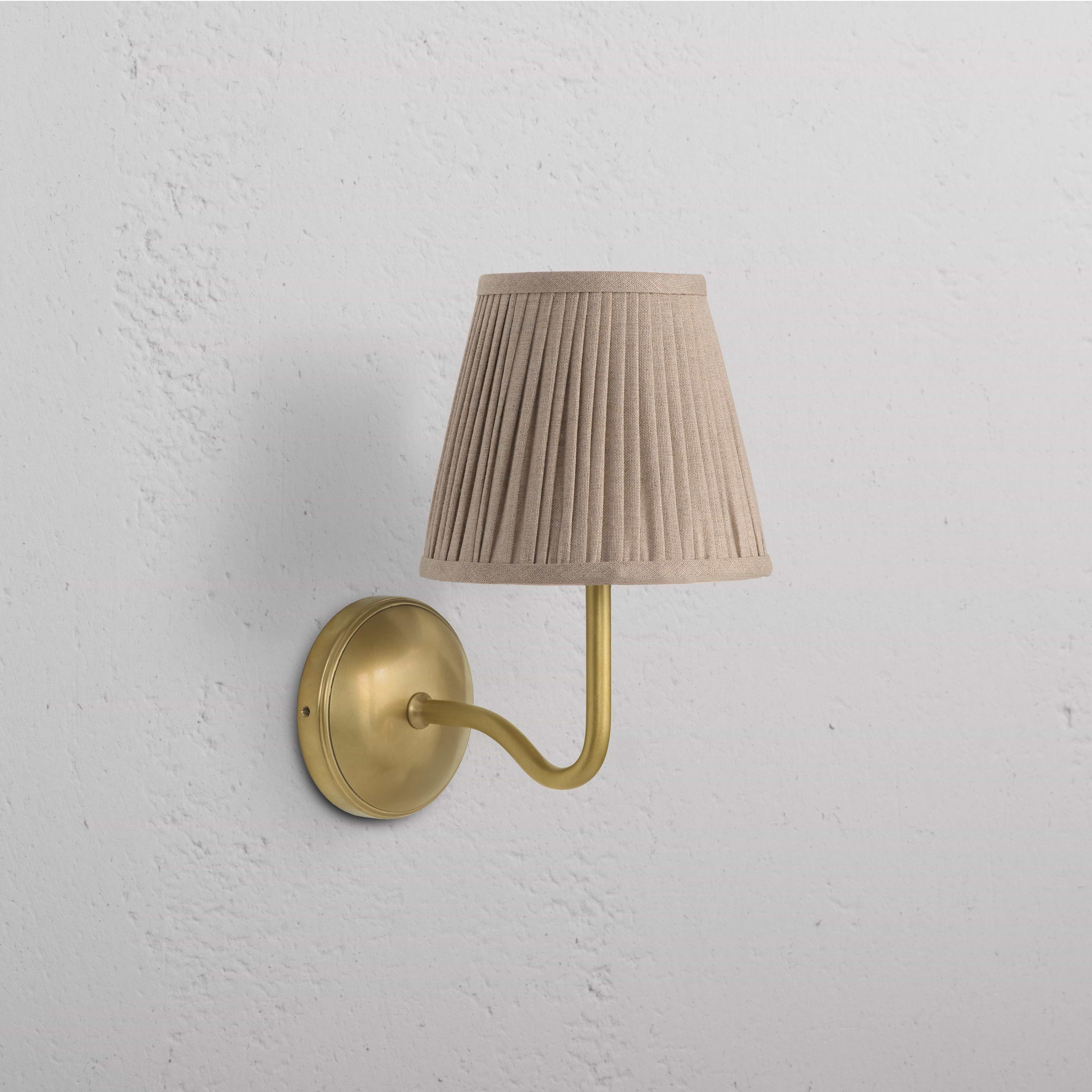 Malvern Medium Wall Light in antique brass with a pleated natural beige shade mounted on a wall.