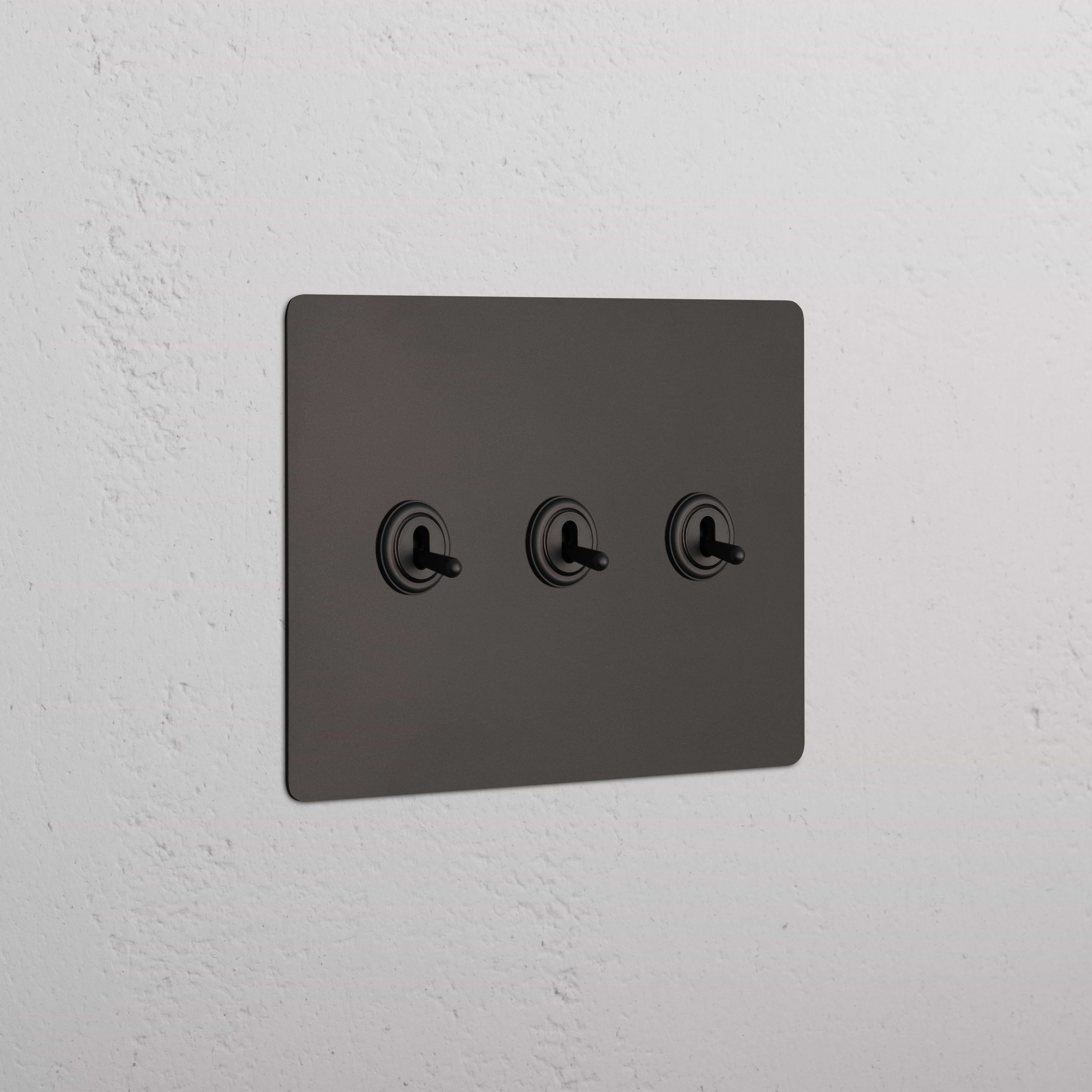 Bronze Kew 3G Toggle Switch with three toggle levers, shown mounted on a wall.