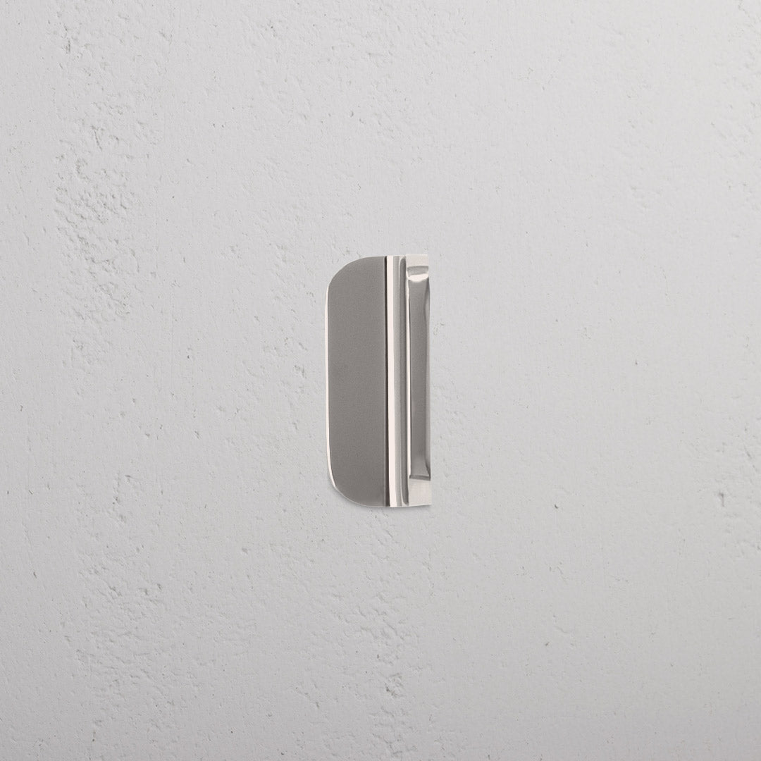 Polished nickel Oxford Furniture Handle Extra Small with rounded edges, mounted on a white textured wall.