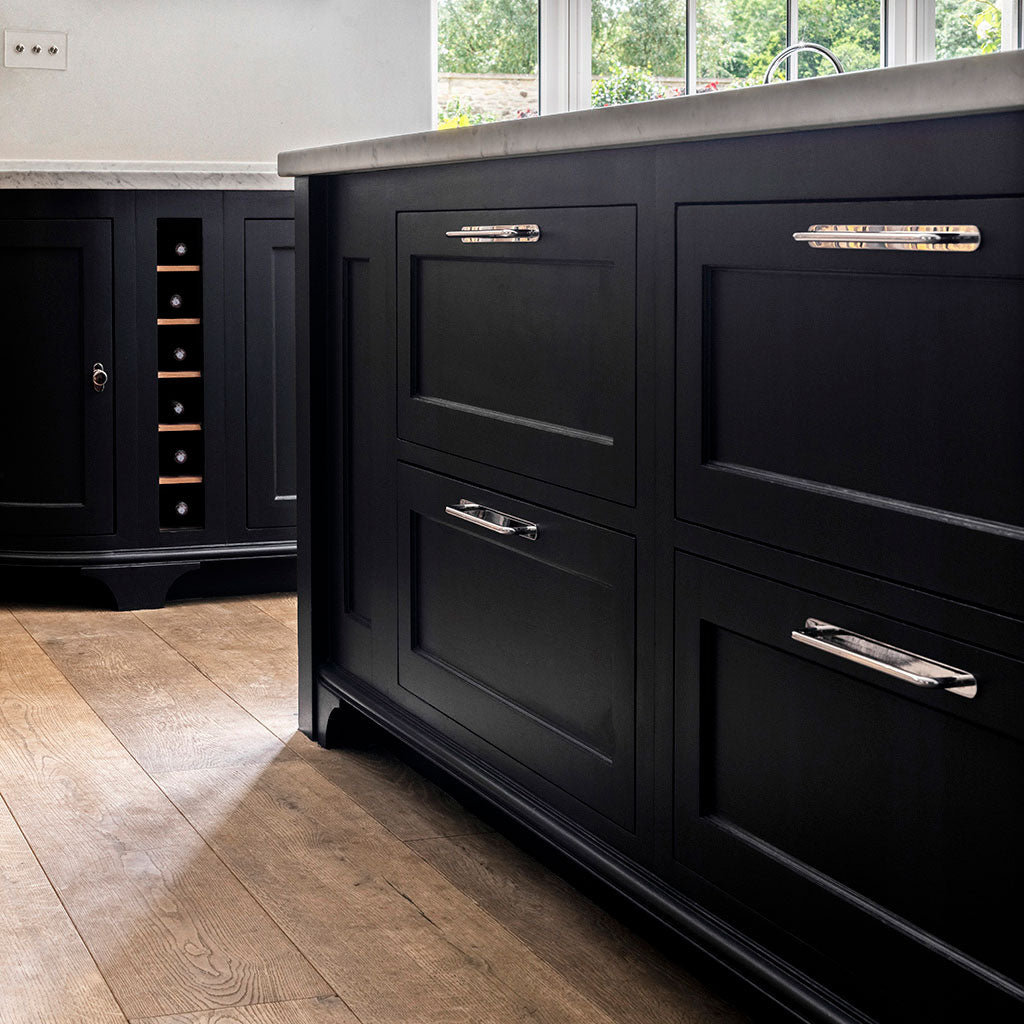 Polished nickel Kilburn Furniture Handle Medium mounted on matte black cabinet drawer in a modern kitchen.