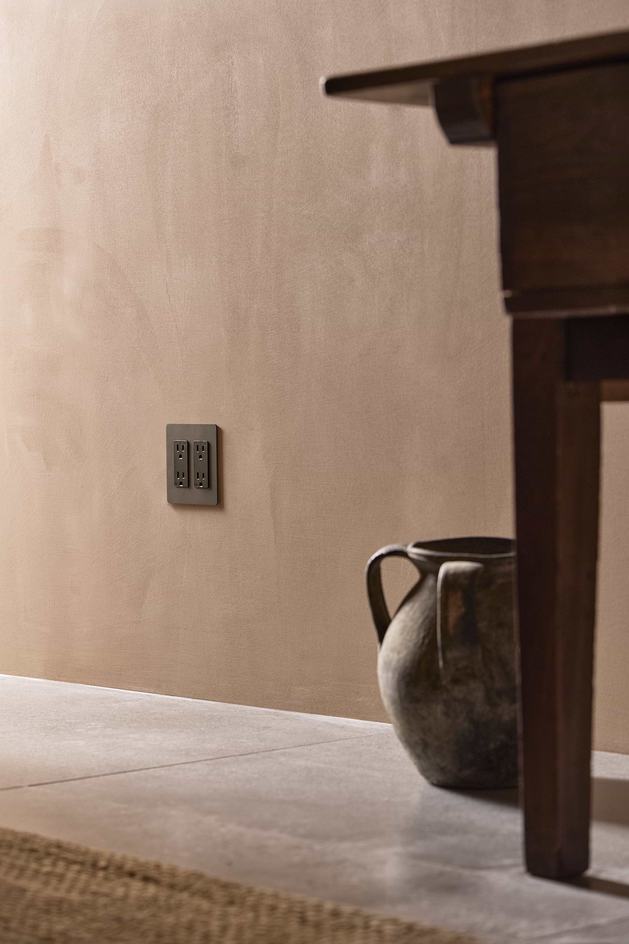 Kew 2G Outlet in Bronze Black mounted on a beige wall, featuring two power sockets.