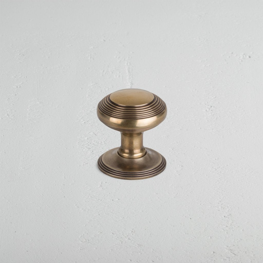 Poplar Passage Door Knob Set in Antique Brass, featuring a round knob with decorative ridges, on a light surface.