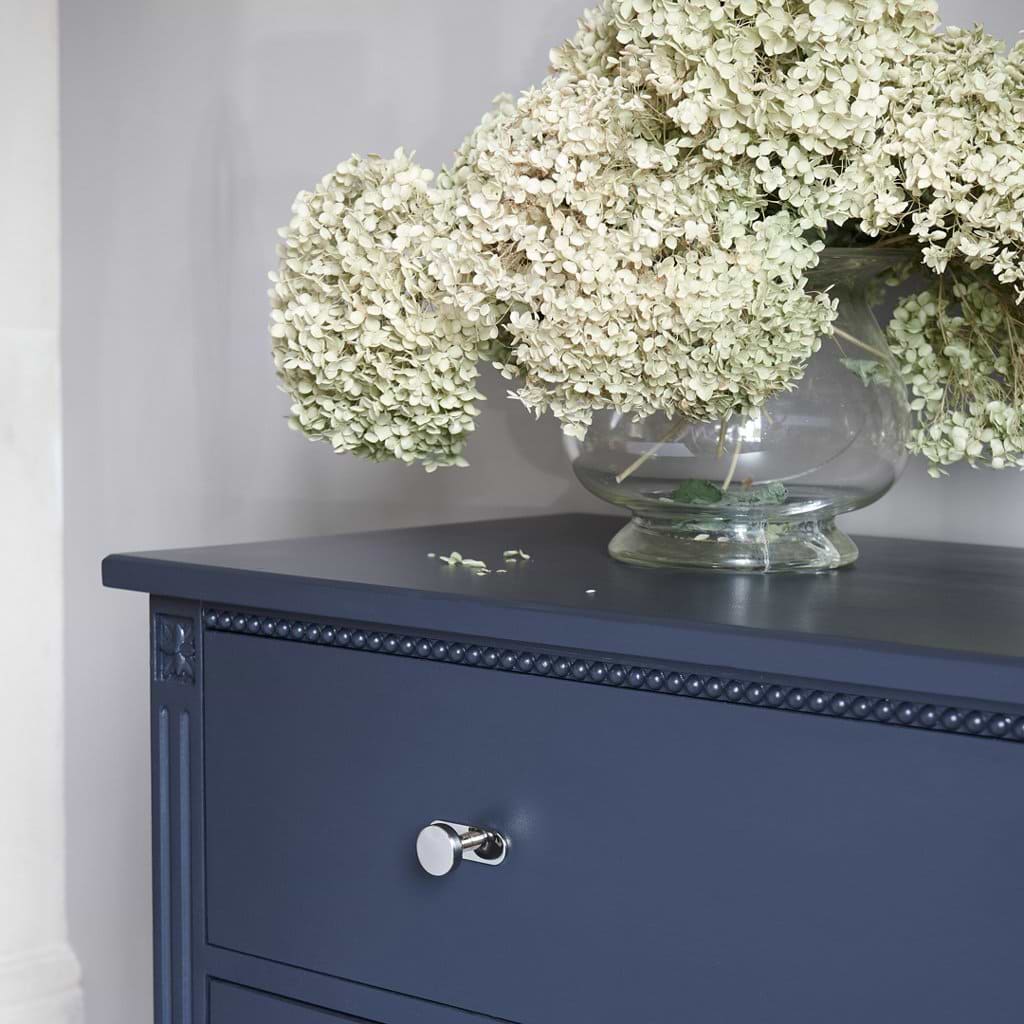 Polished nickel Kilburn Furniture Knob fitted on a dark blue dresser against a light gray wall.