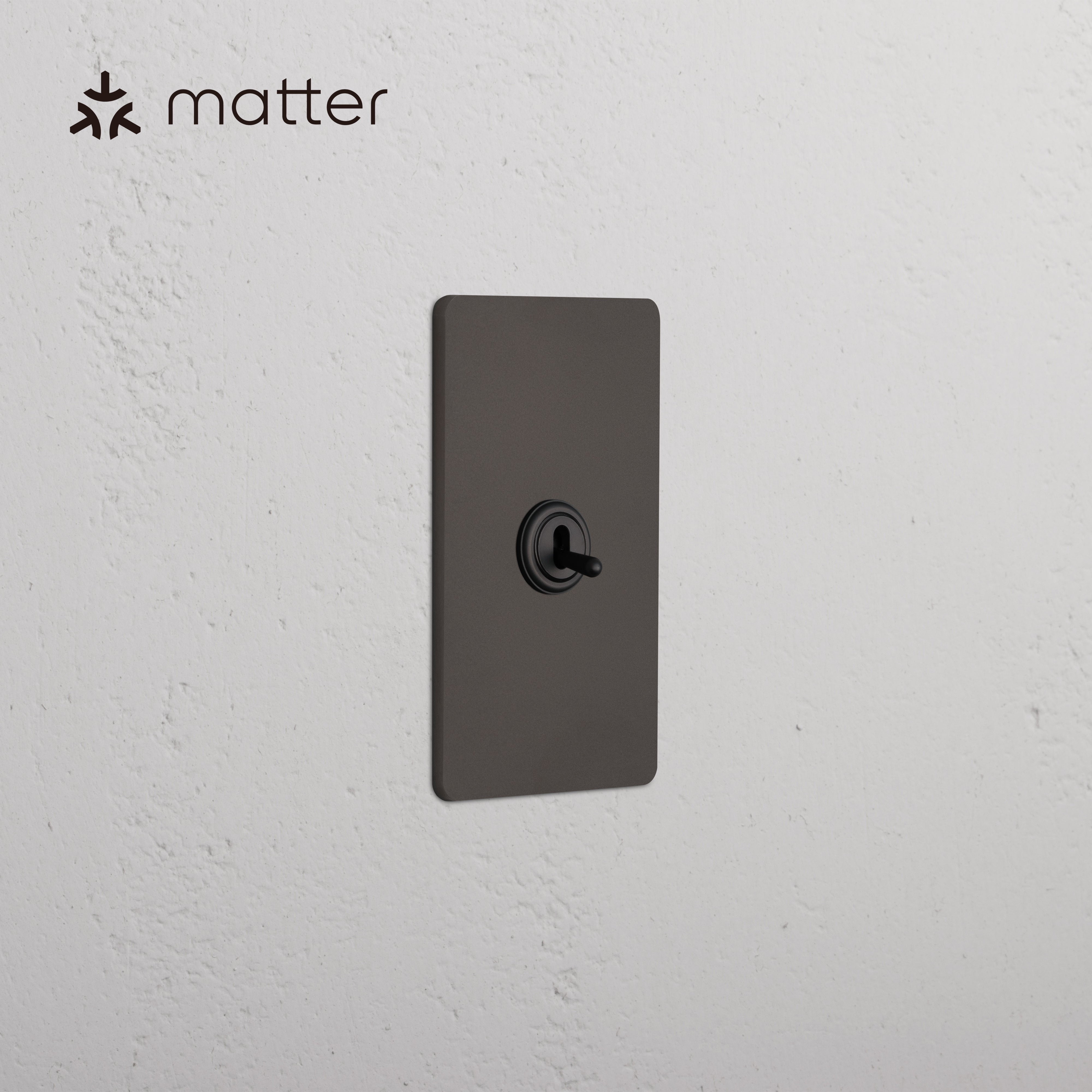 Grove 1G Smart Retractive Toggle Switch in bronze finish, shown mounted on a white textured wall.