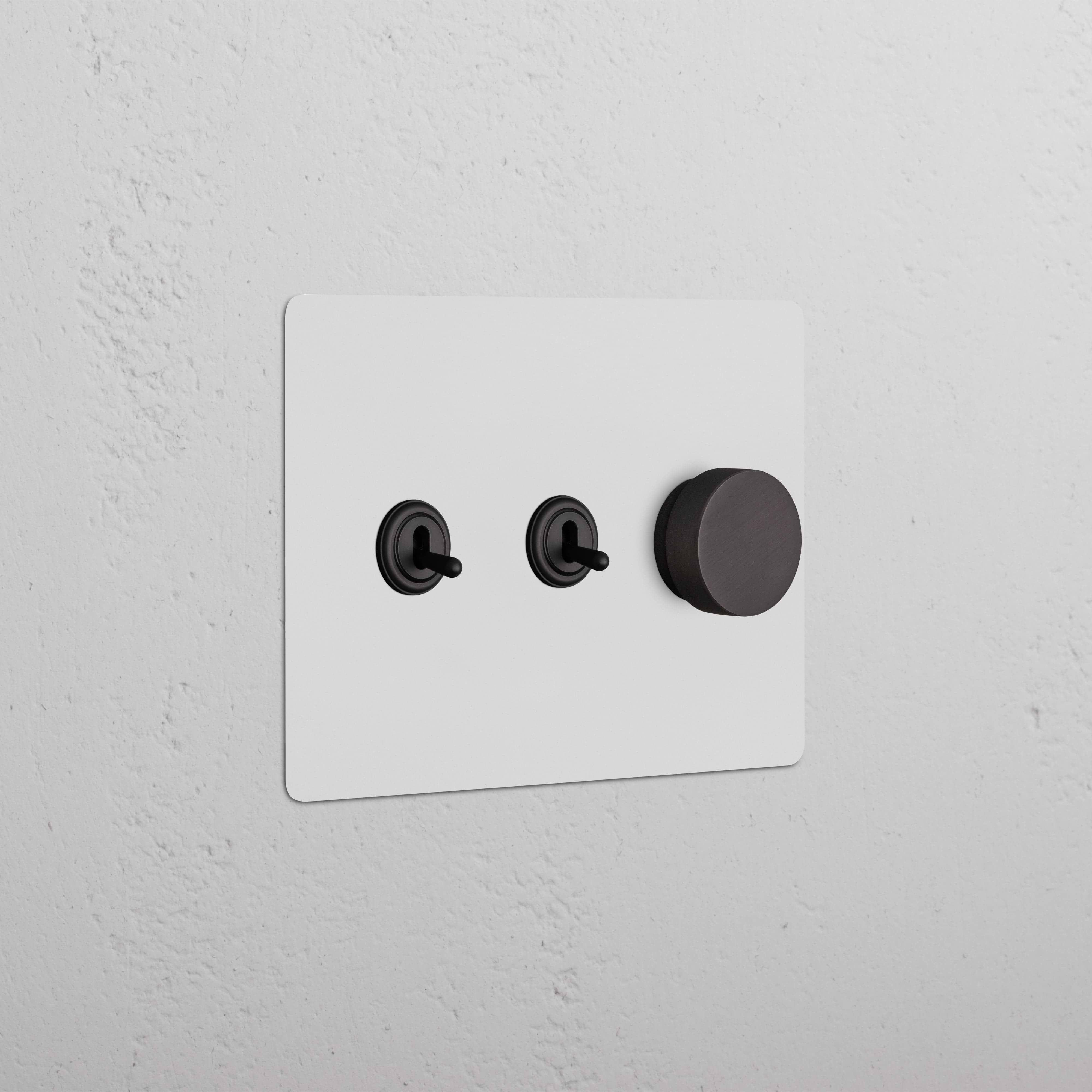 Kew 3G 2x Toggle & Dimmer Switch in paintable bronze with two toggles and one dimmer knob on a wall.