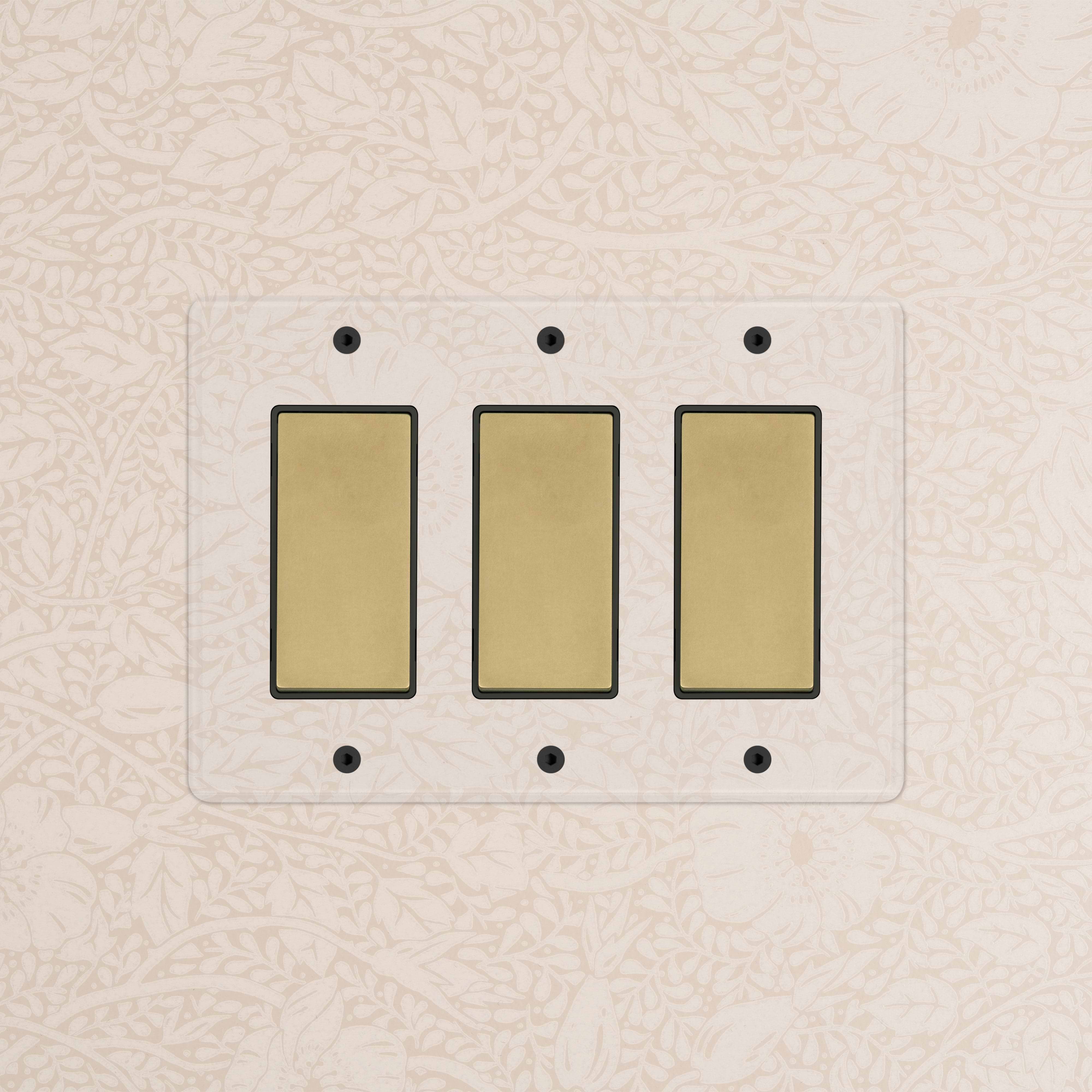 Kew 3G Rocker Switch in Clear Antique Brass with Black rockers, mounted on a light-colored wall.