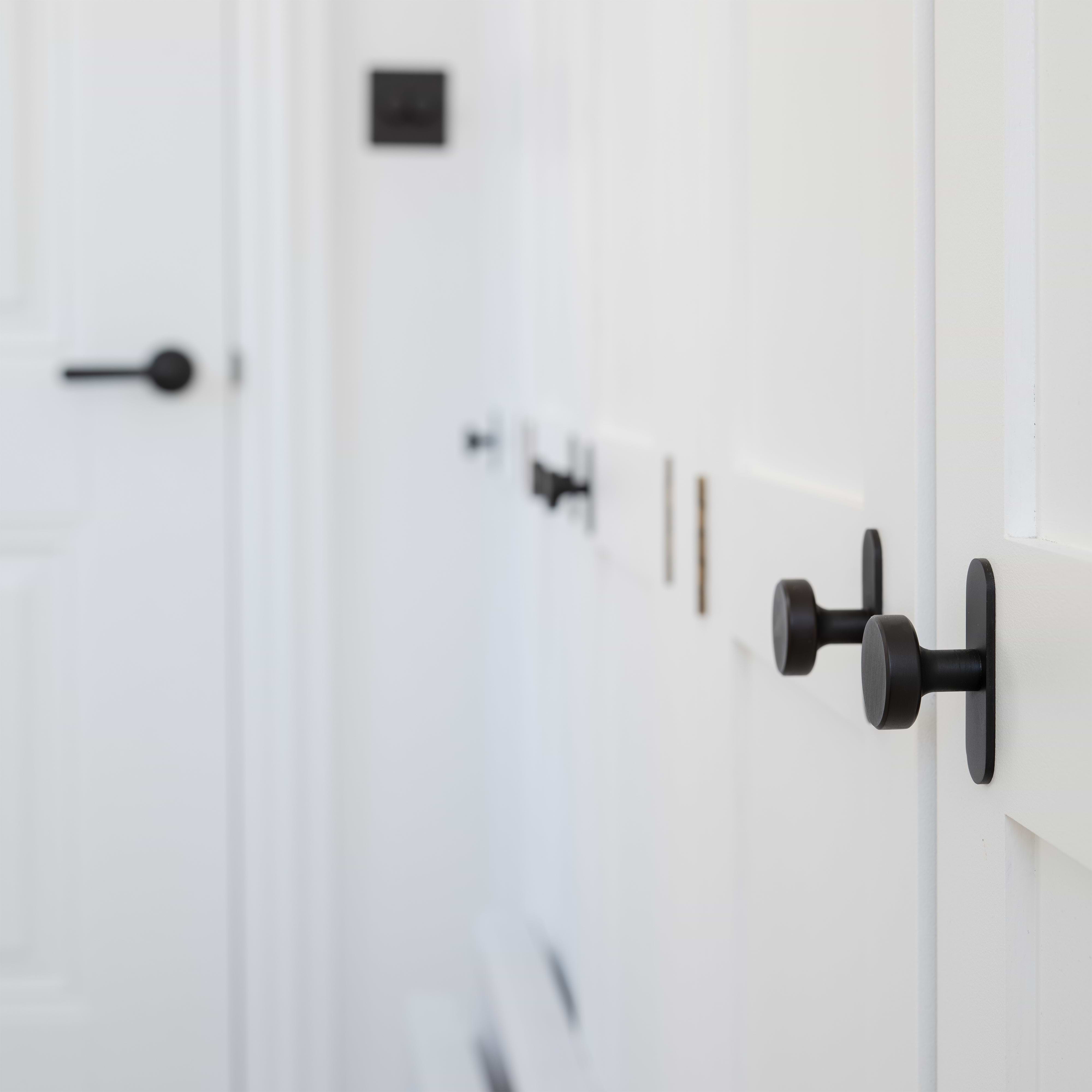 Close-up of a bronze Kilburn Furniture Knob mounted on a white cabinet in a bright, minimalistic space.