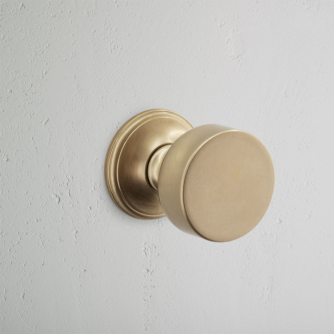 Onslow Passage Door Knob Set in Antique Brass mounted on a light grey textured wall.