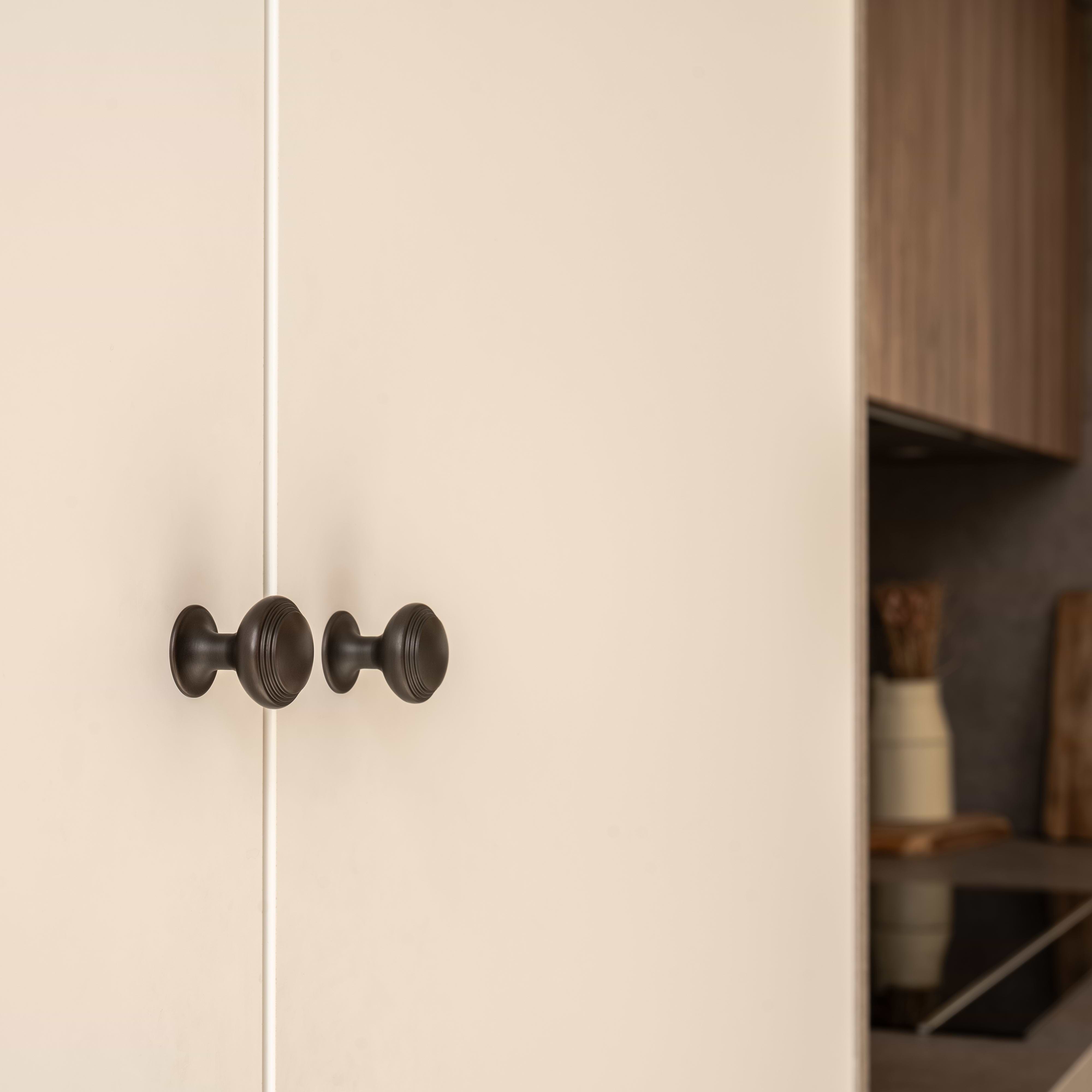 Close-up of two Barlow Furniture Knob Small in bronze mounted on cream-colored cabinet doors.
