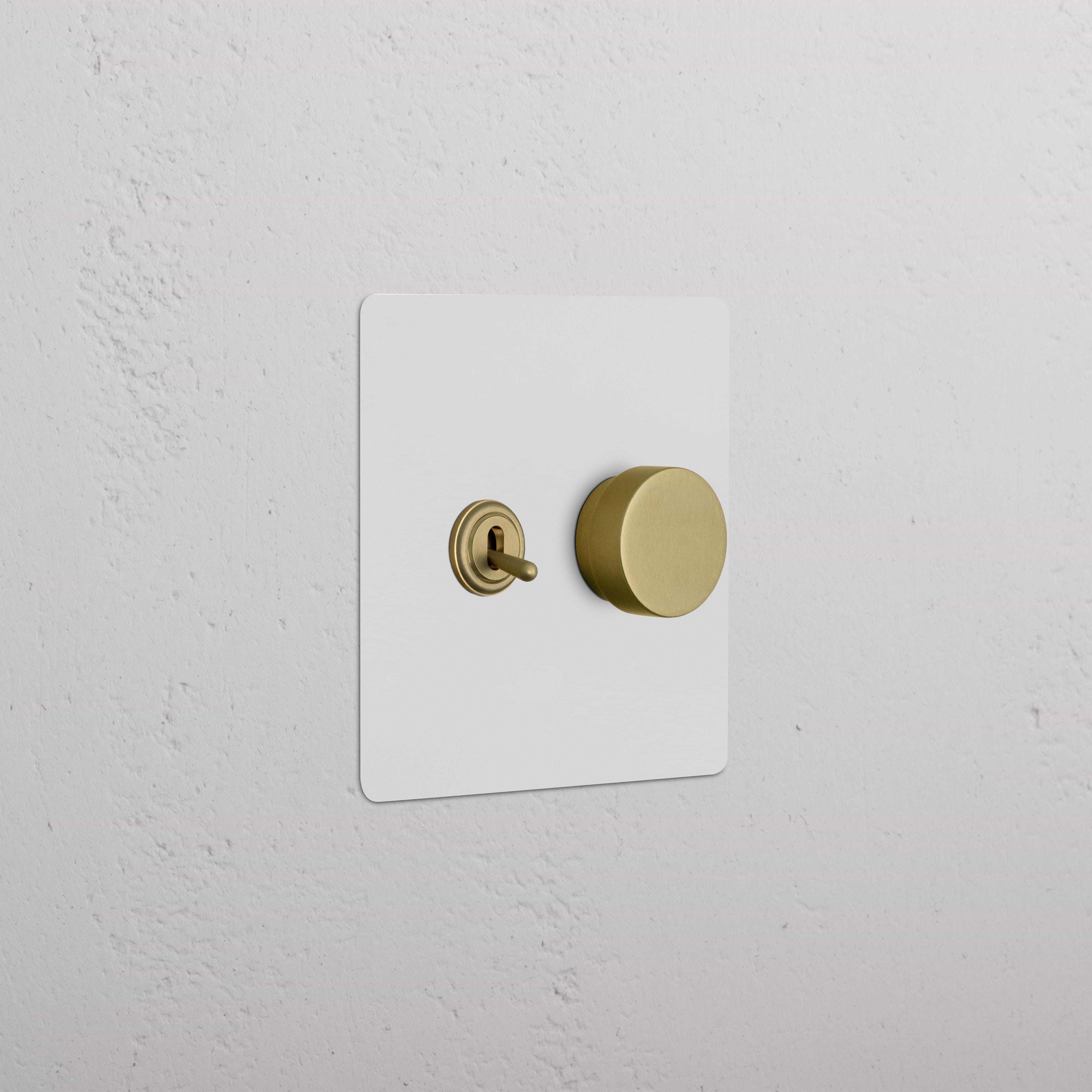 Kew 2G Toggle & Dimmer Switch in paintable antique brass finish, shown on a textured white wall.