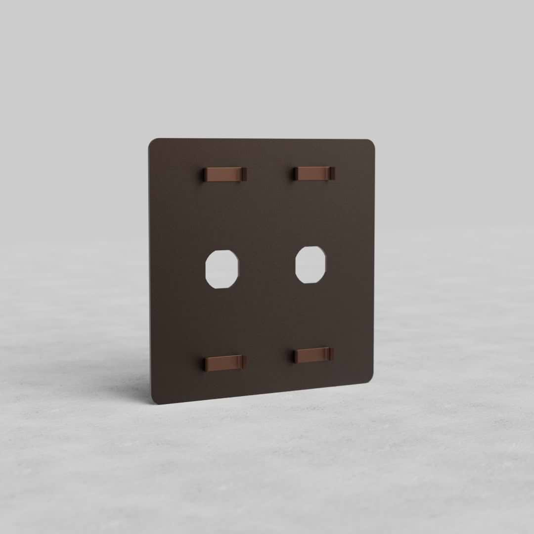 Bronze 2G switch plate 'Kew US' with two rectangular switch cutouts, displayed upright on gray surface.