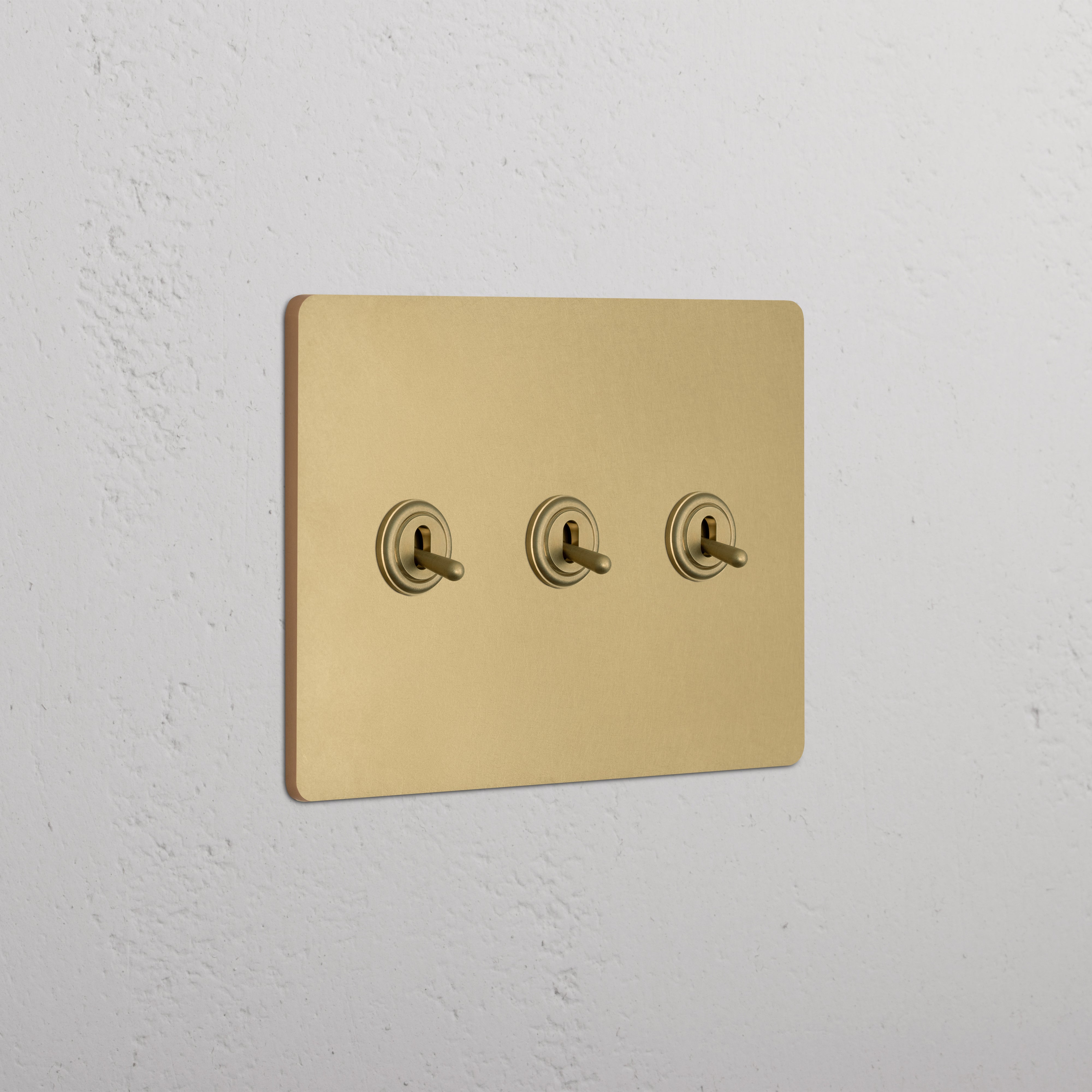 Grove 3G Toggle Switch in antique brass with three gold-colored toggle switches on a white wall.